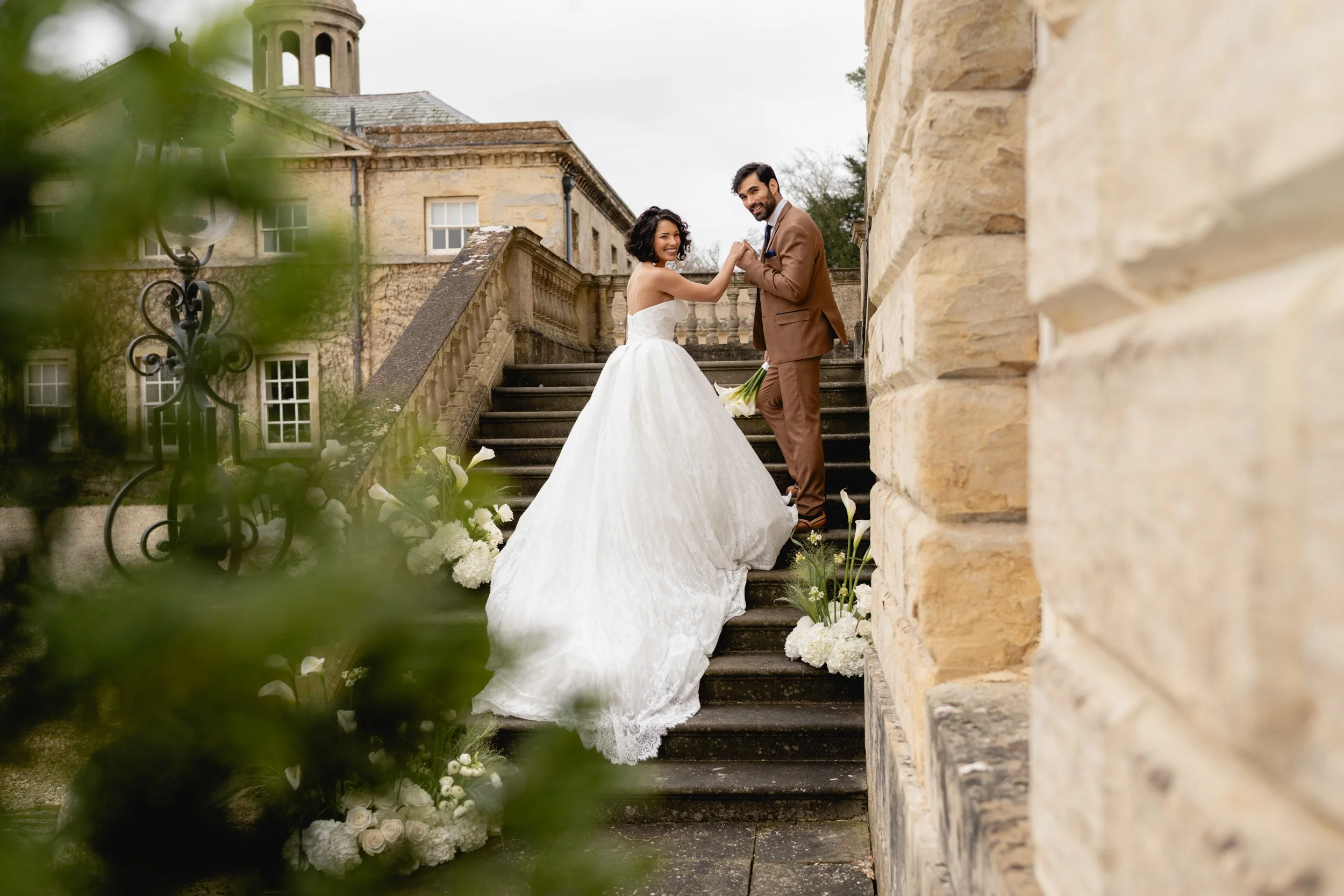 Bride and groom  looking back toward the camera while holding hands on the front steps of  Kirtlington Park in Oxfordshire