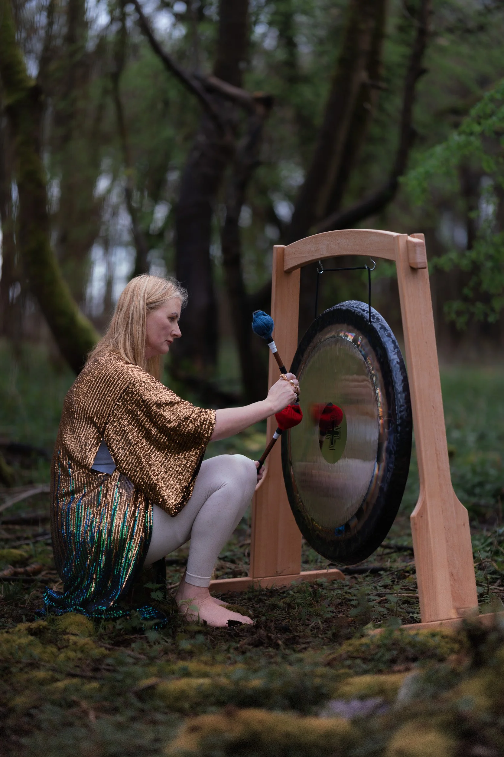 Sound healer playing a gong suring a sound healing session in the woodland near Amersham Buckinghamshire for a brand photoshoot