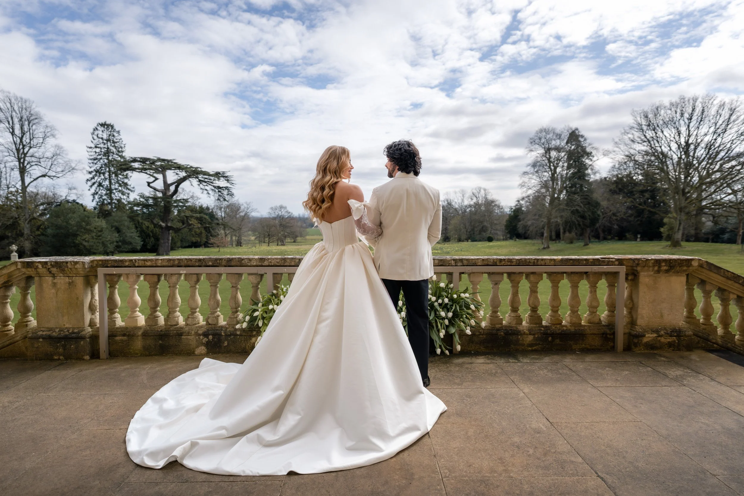 Bride and groom overlooking the gardens from a balcony at Kirtlington Park in Oxfordshire