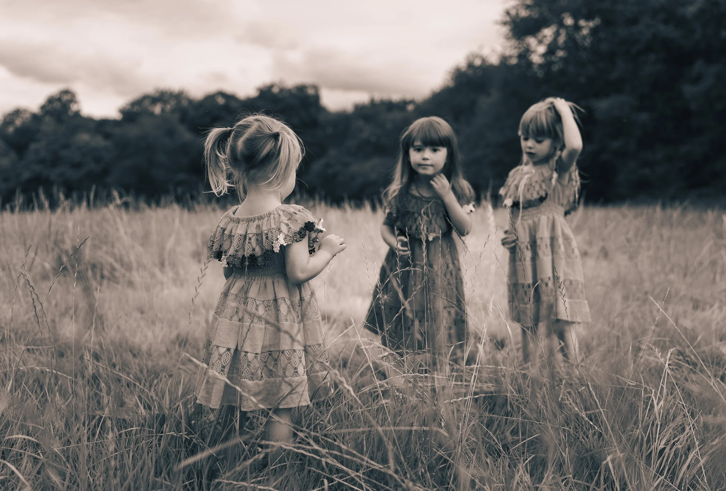 Three young sisters standing together in long grass during an outdoor family session in Buckinghamshire