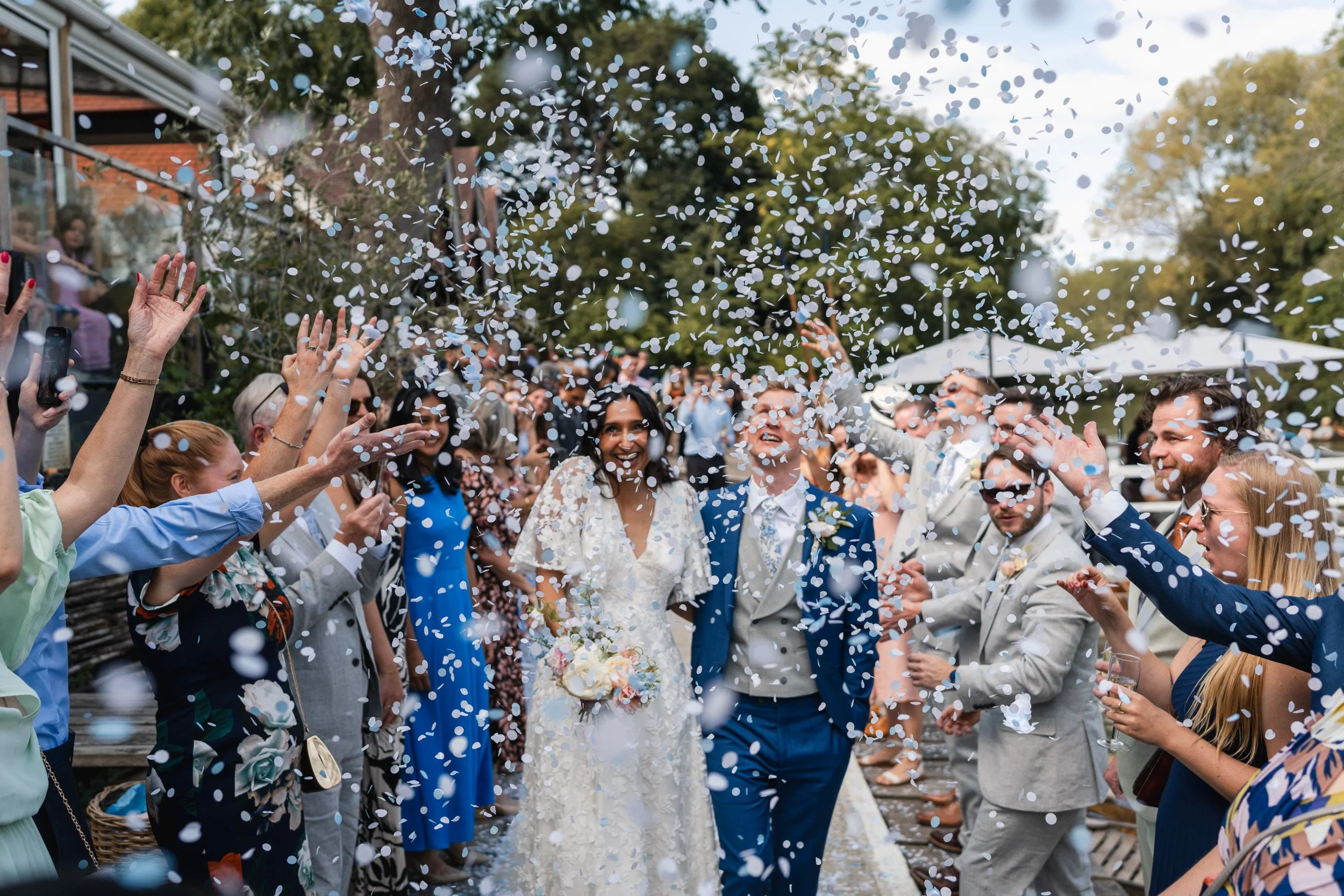 Bride and groom walking through a joyful confetti throw outside Cherwell Boathouse in Oxford