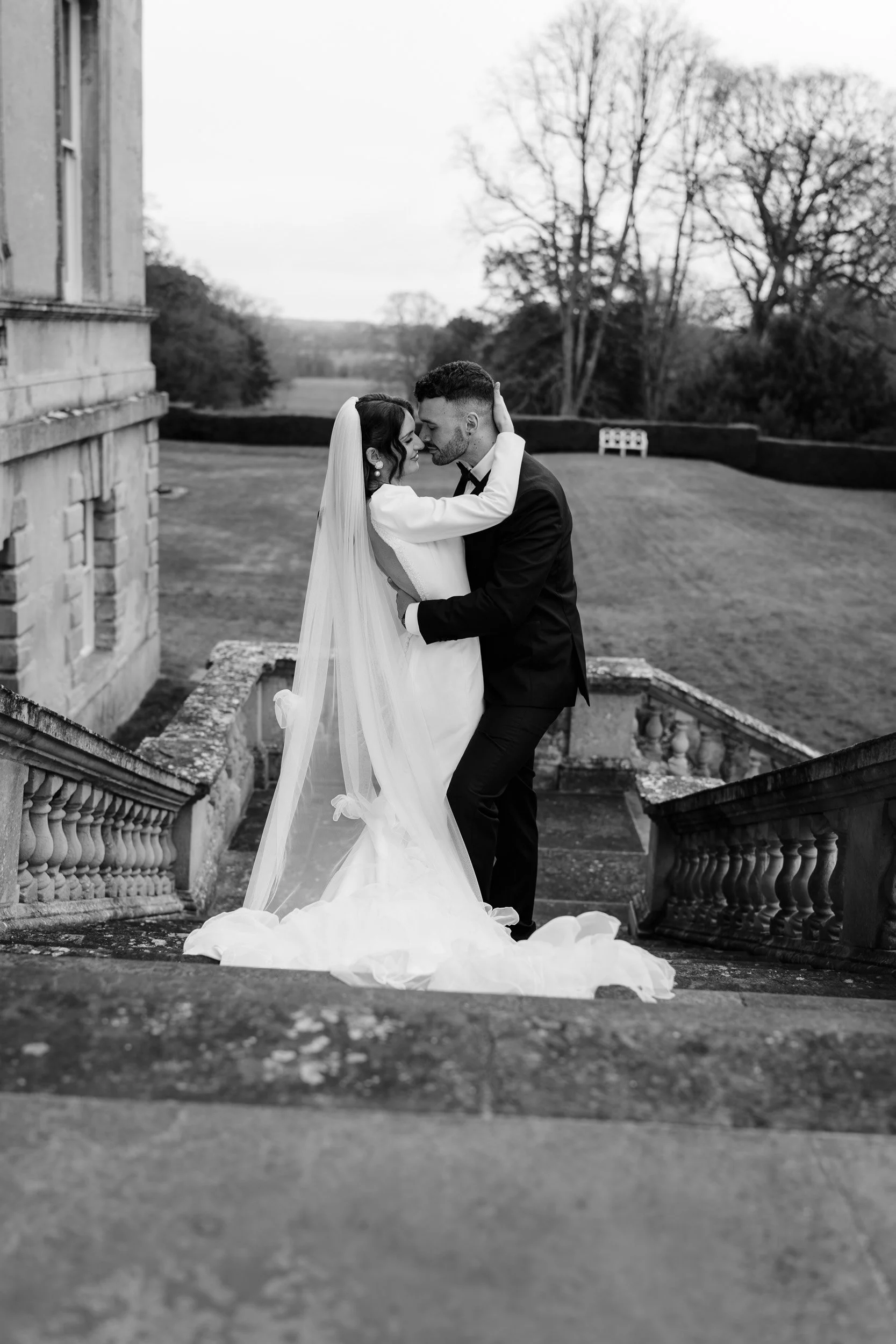 Bride and groom pausing to kiss on garden steps at Kirtlington Park in Oxfordshire
