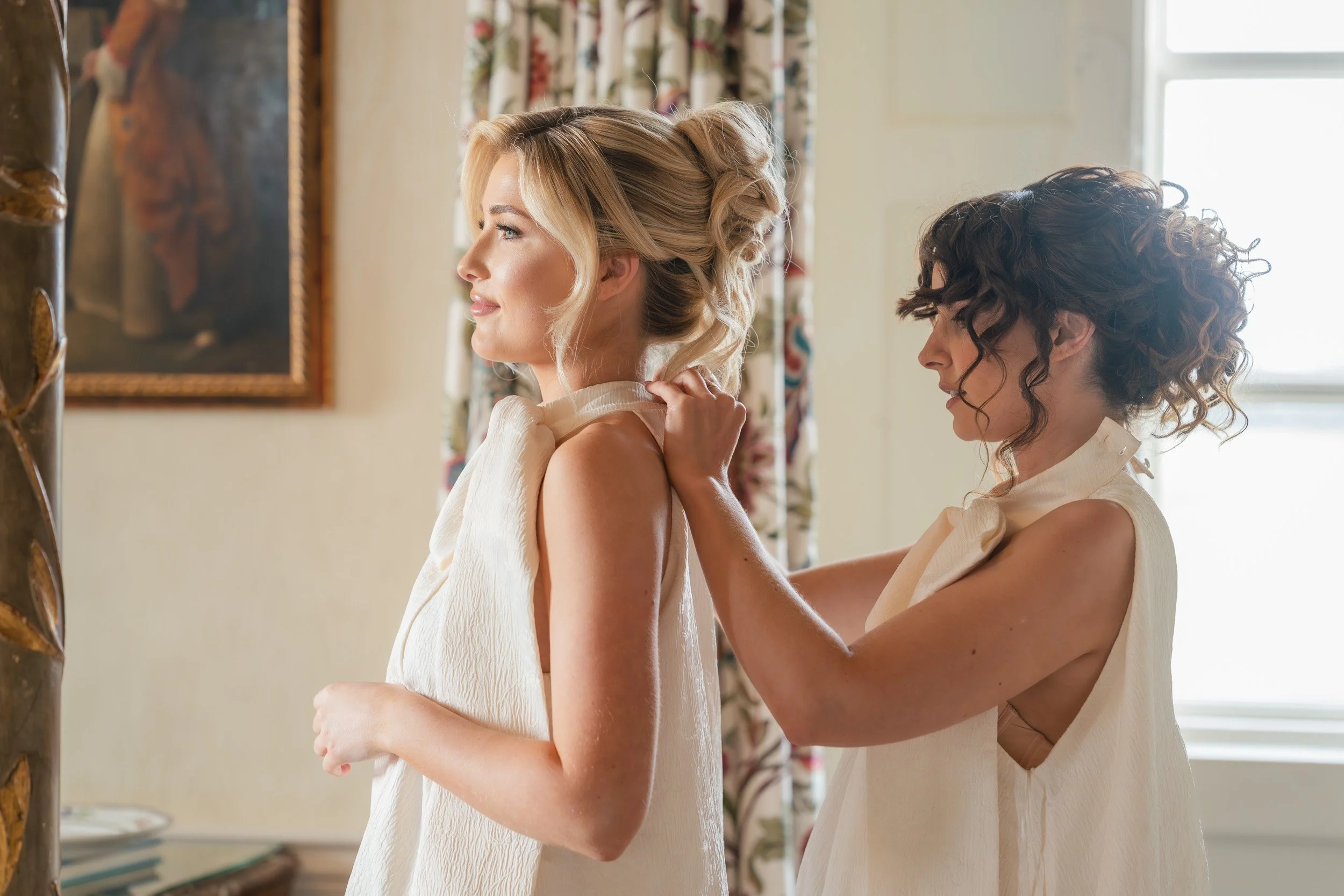 Bridesmaids helping each other get dressed in the bridal suite at Kirtlington Park in Oxfordshire