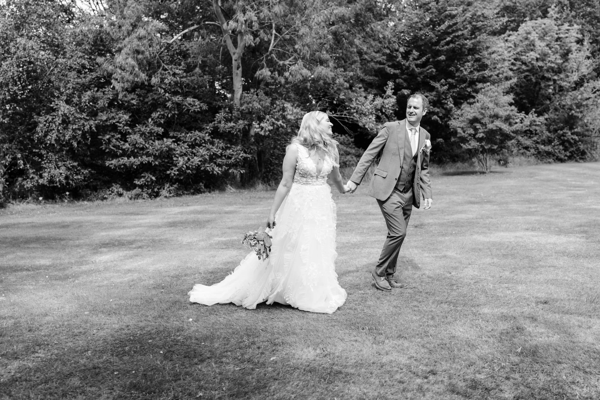 Black and white wedding portrait of the newly weds walking hand in hand through the grounds of Wasing Park after their outdoor ceremony