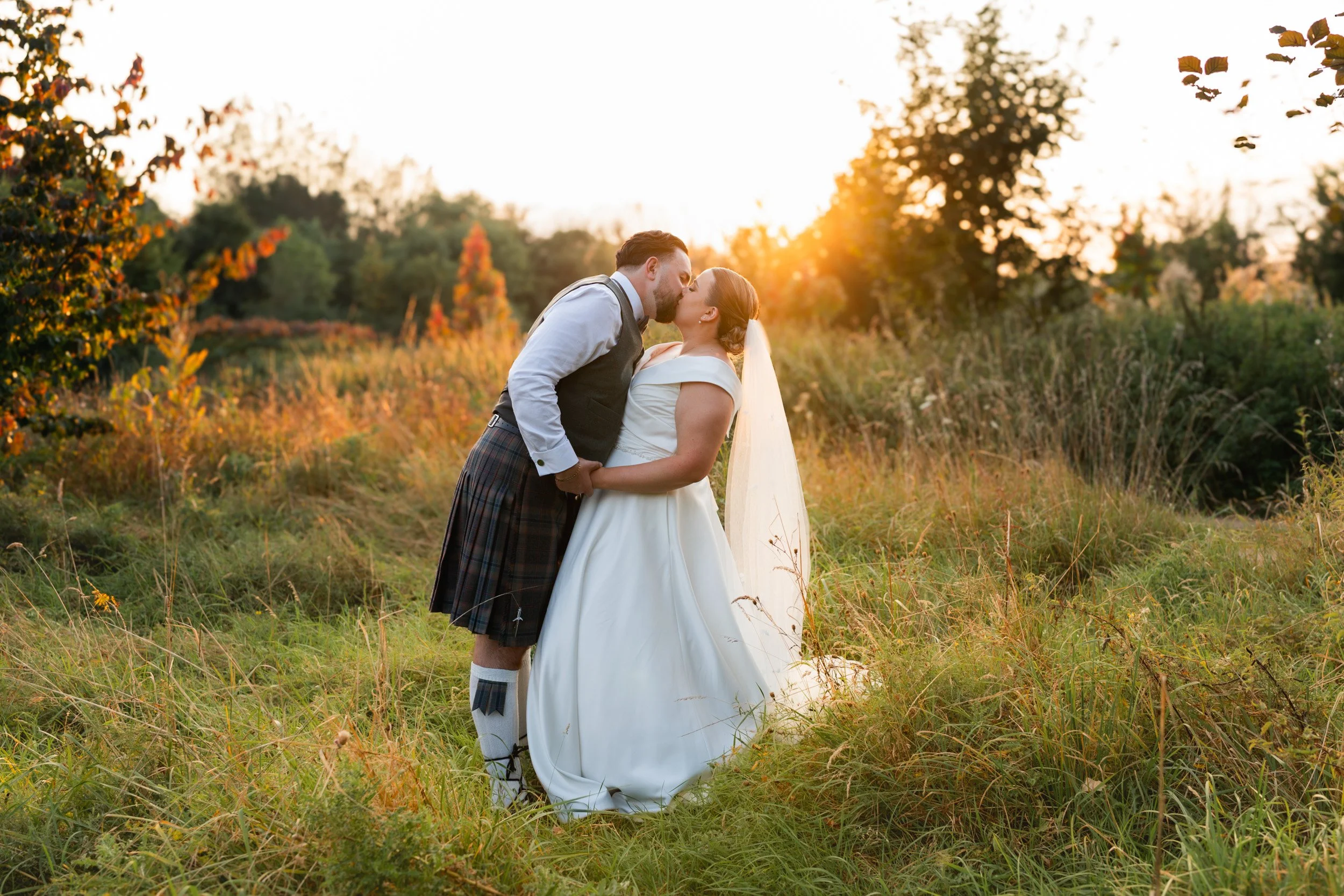 Bride and groom kissing in the golden hour light at their Rivervale Barn wedding venue in Hampshire