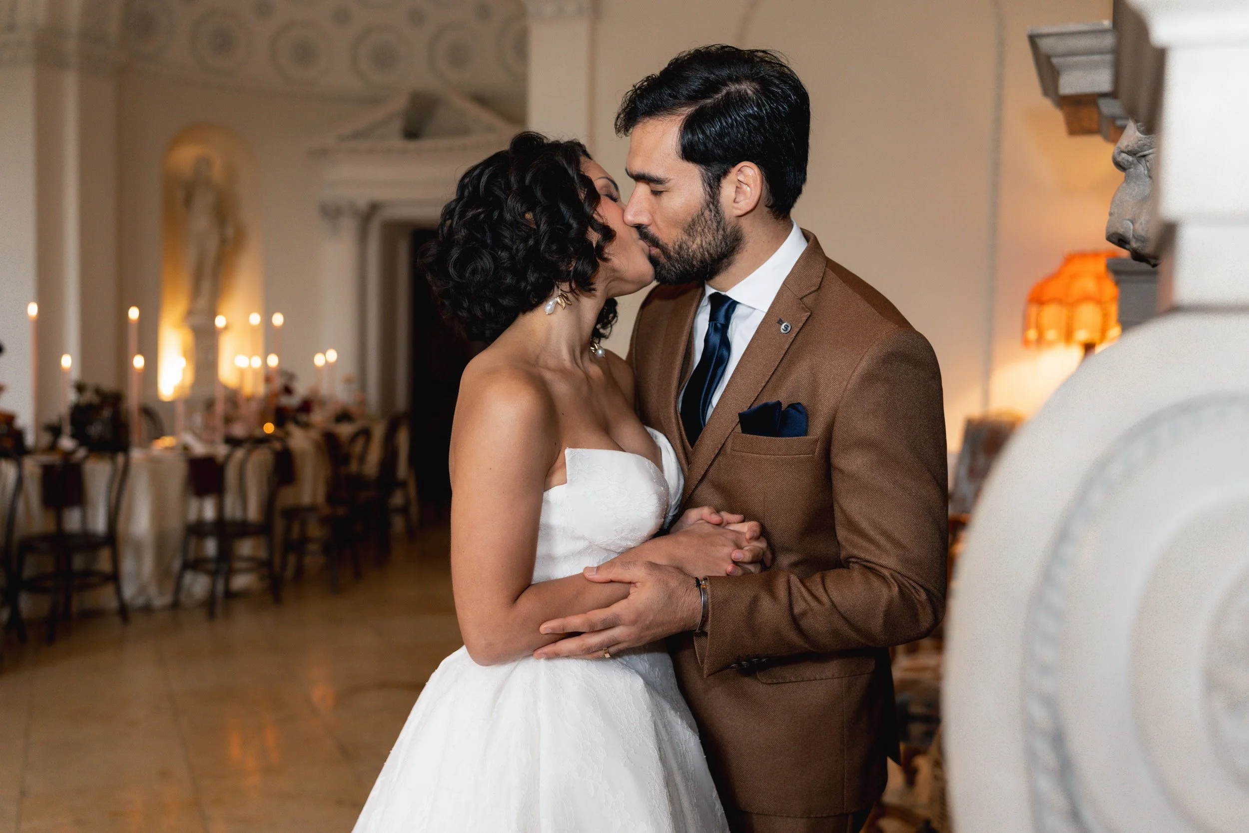 Bride and groom sharing a kiss in front of a fireplace at wedding reception at Kirtlington Park in Oxfordshire