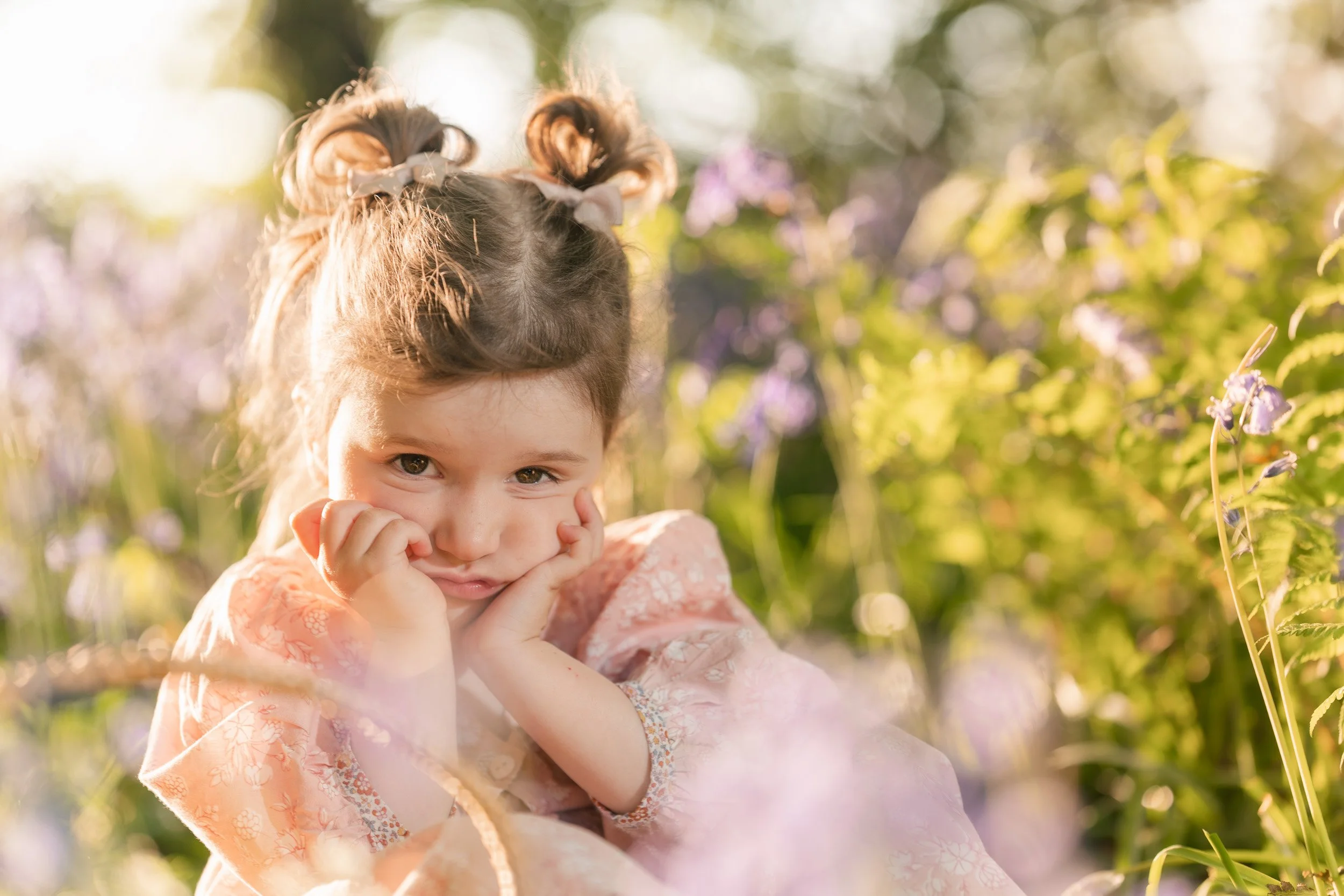 Toddler girl sitting among the flowers during bluebell season in the Chiltern Hills  near Amersham, Buckinghamshire during a family photography session 