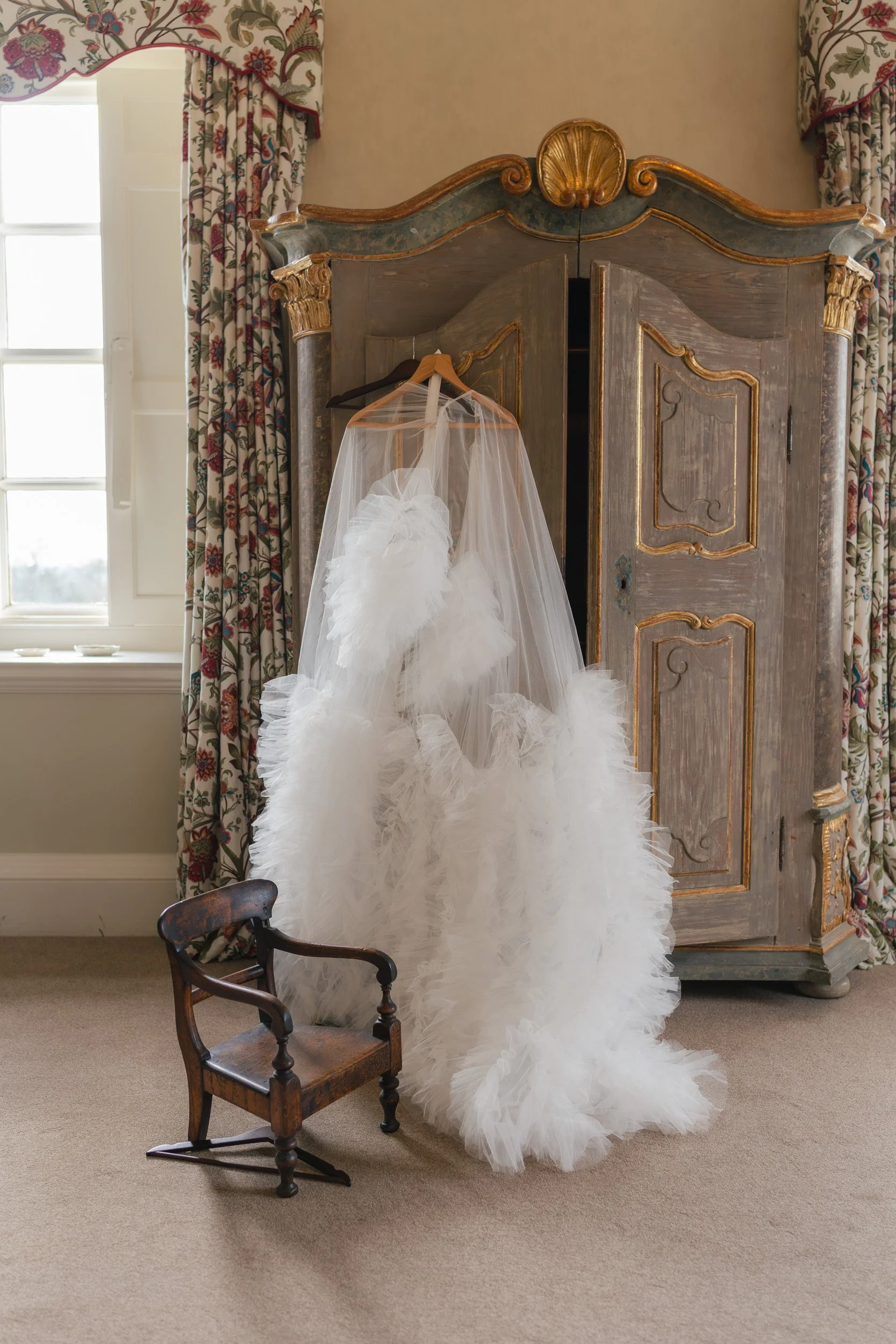 Wedding dress hanging on the antique furniture in the bridal suite at Kirtlington Park in Oxfordshire