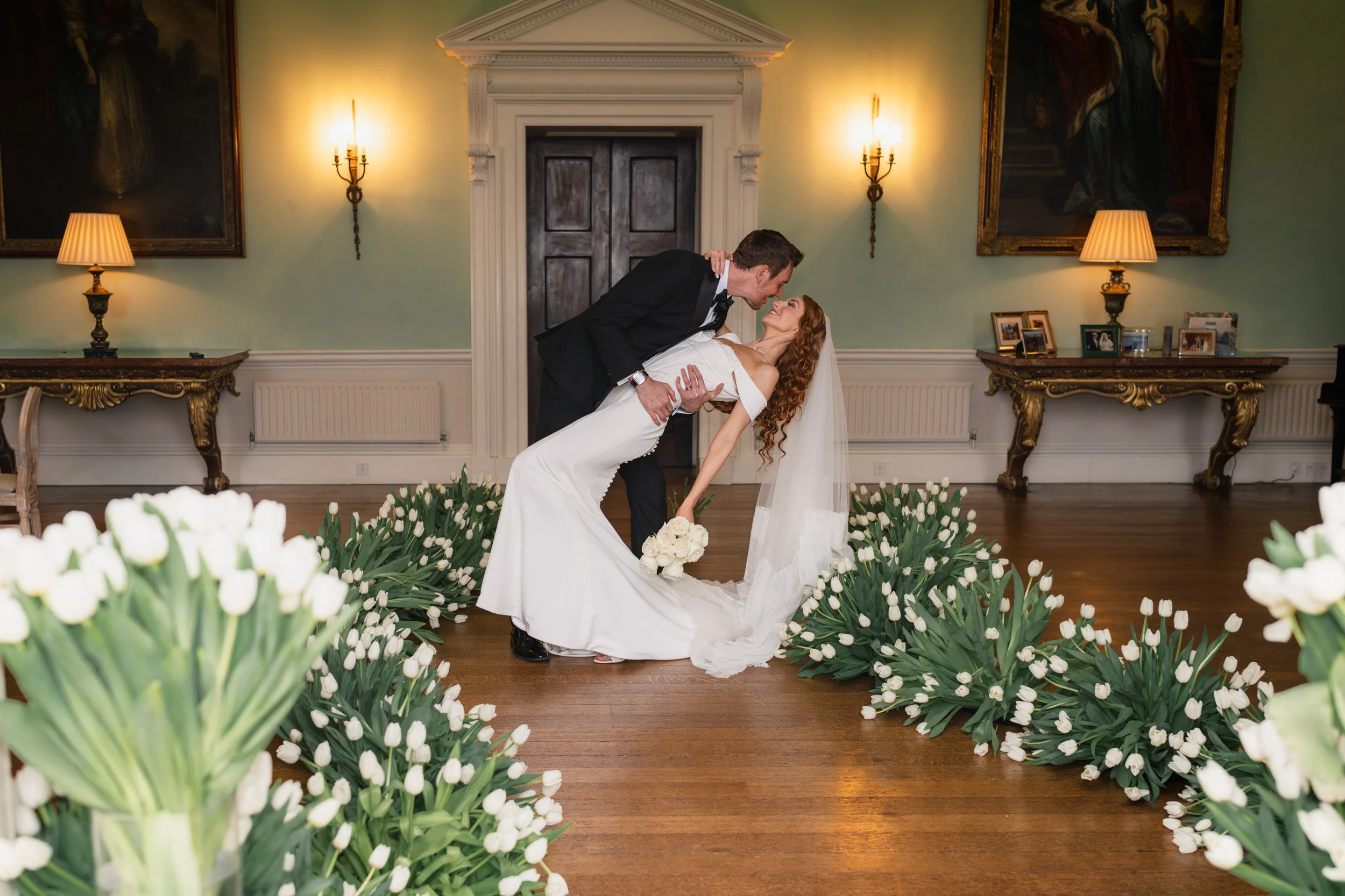 Groom dipping his bride for a kiss in a tulip-lined aisle during their reception at Kirtlington Park in Oxfordshire