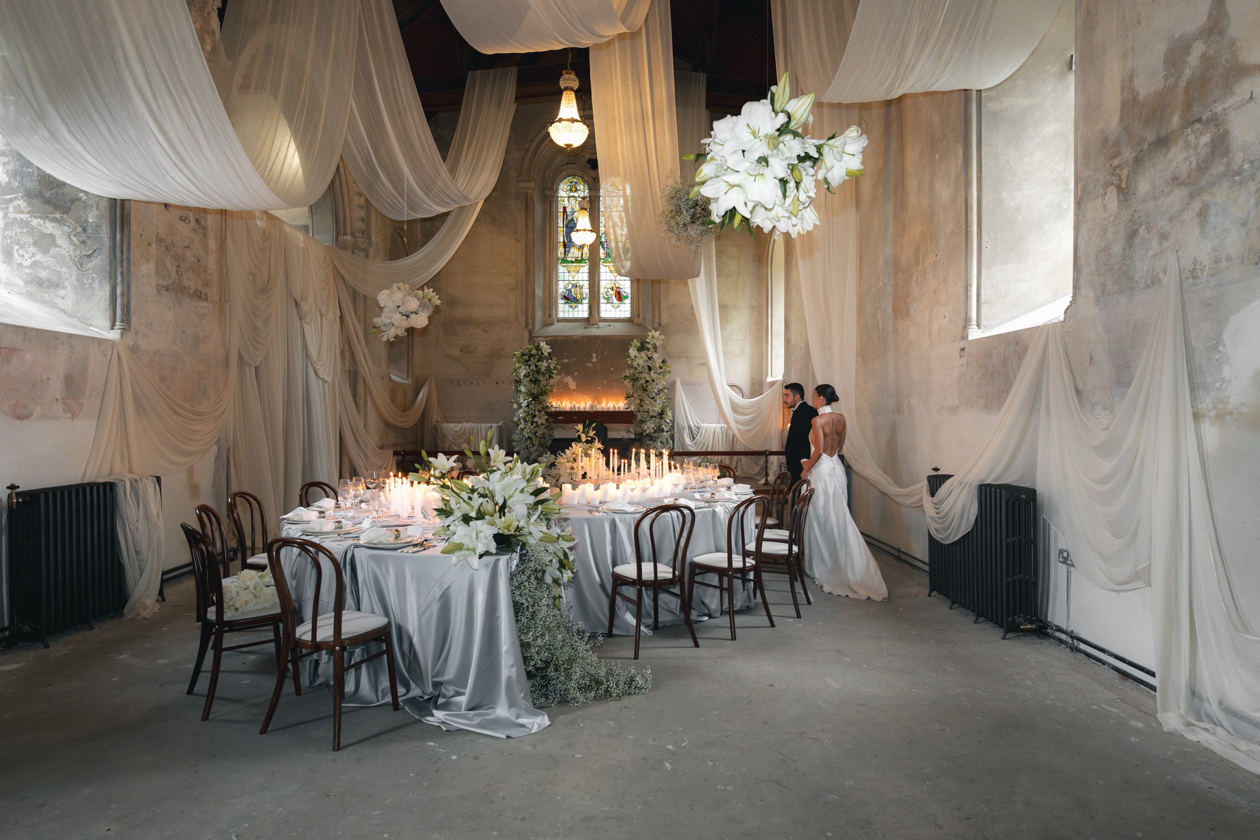 Bride and groom close as they walk through their candlelit reception room with draped fabric and floral displays inside The Bell Tower at The Elvetham Hotel in Hampshire