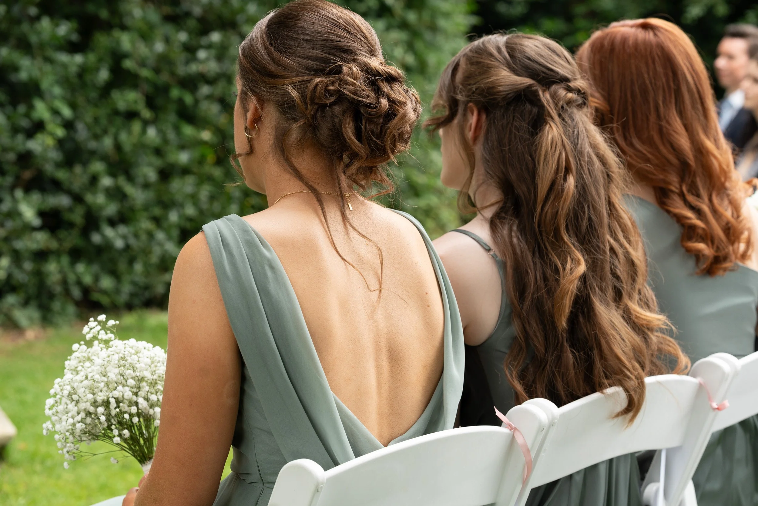Bridesmaids sitting together holding their bouquets and watching as the bride and groom say I do at an outdoor garden ceremony  Wasing Park in Berkshire