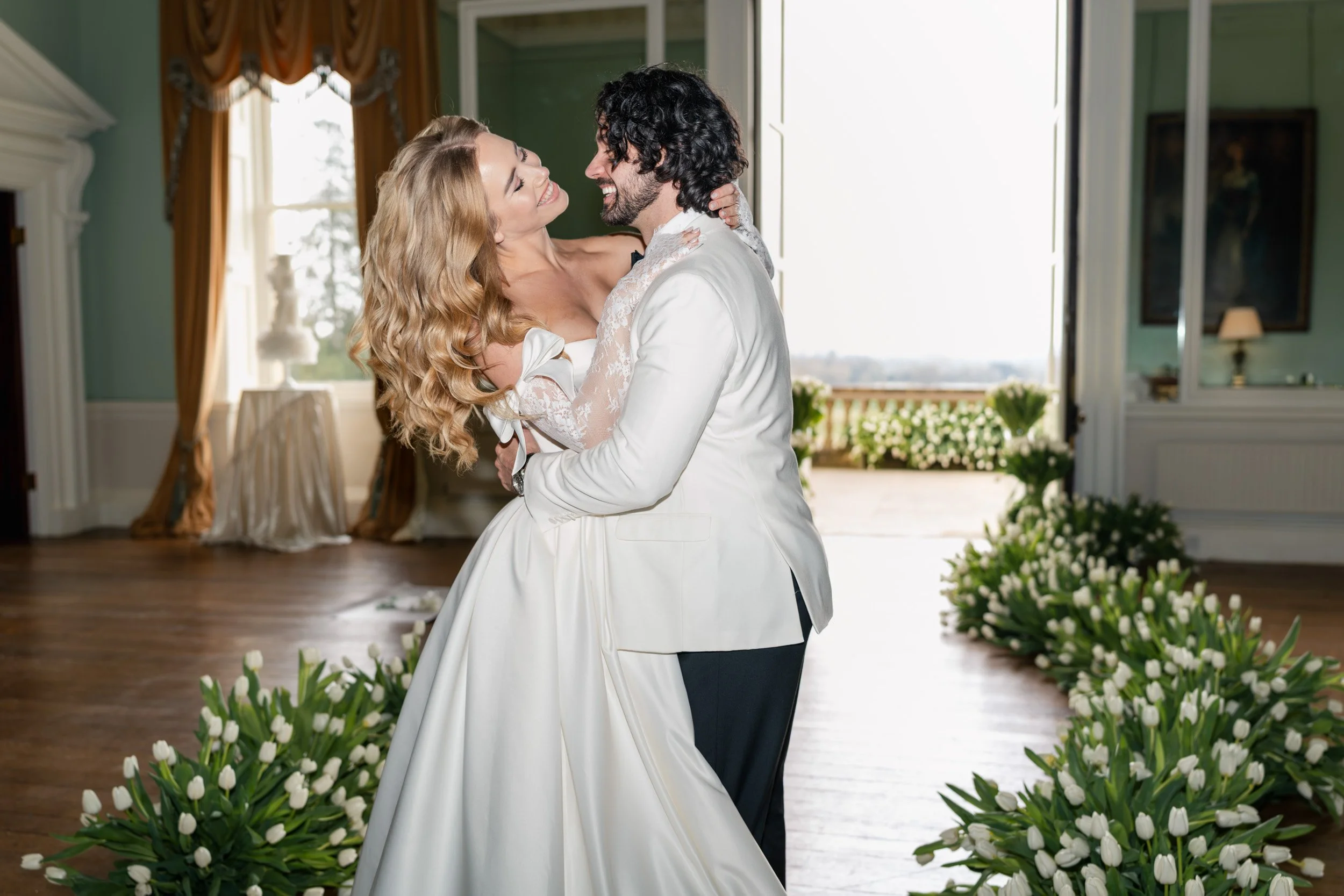 Groom playfully kissing his bride on the neck in a tulip-lined aisle during their reception at Kirtlington Park in Oxfordshire