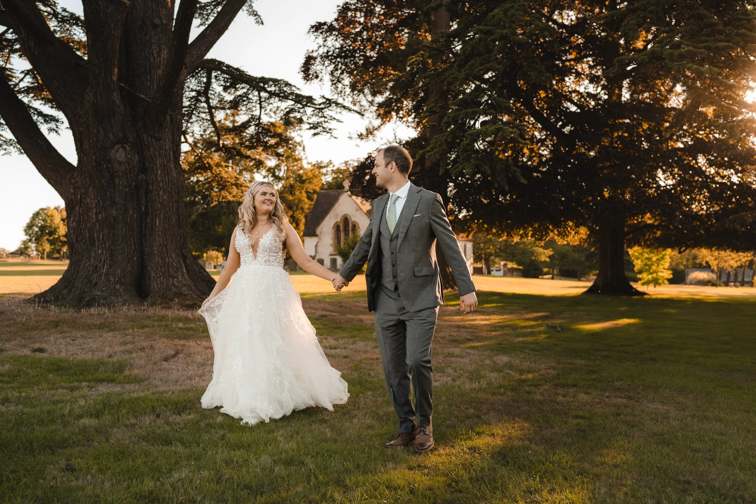 Bride and groom holding hands and walking  in the golden sunset light in the meadows of Wasing Park in Berkshire