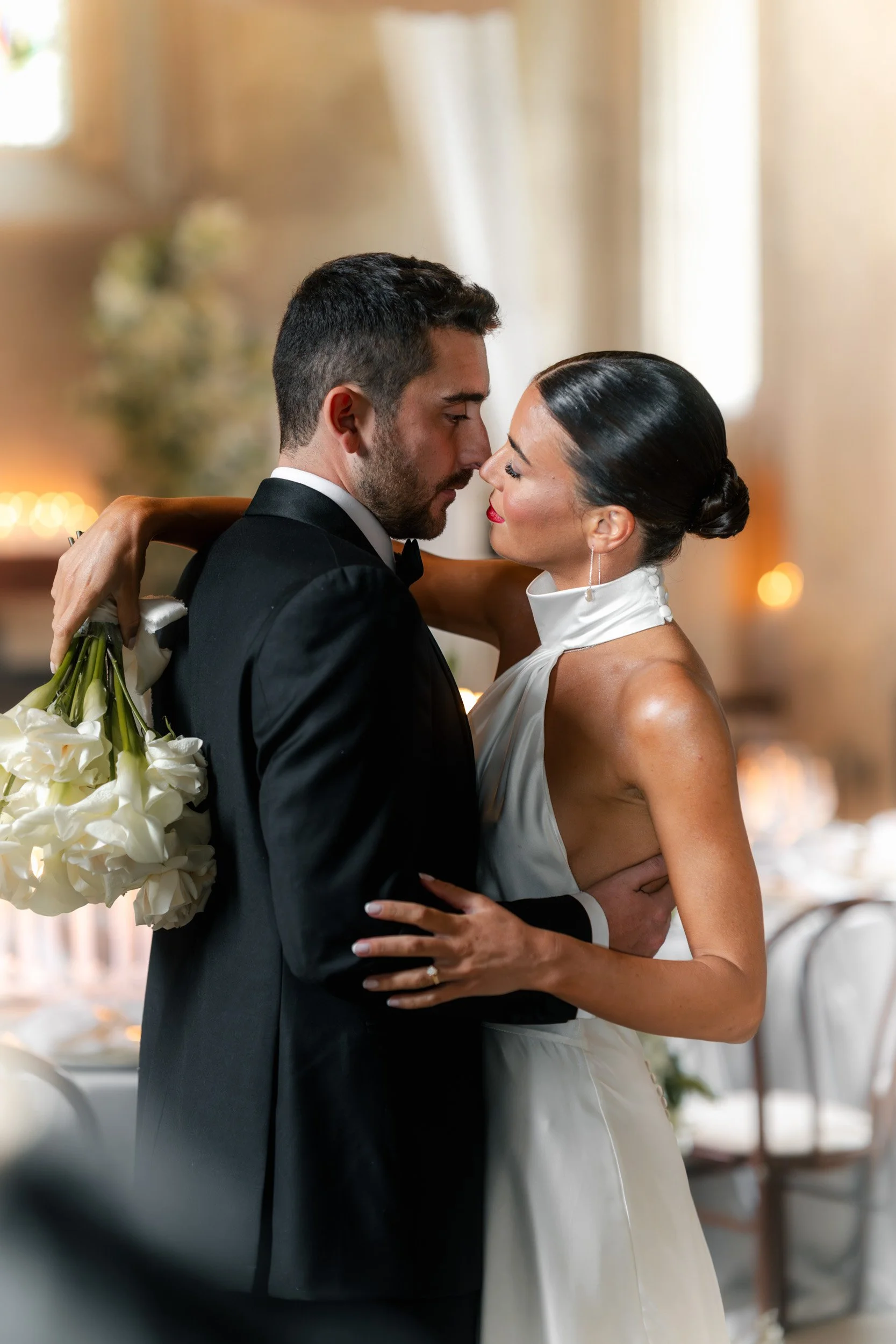 Close up of a bride and groom embracing in  a candlelit reception room with draped fabric and floral displays inside The Bell Tower at The Elvetham Hotel in Hampshire
