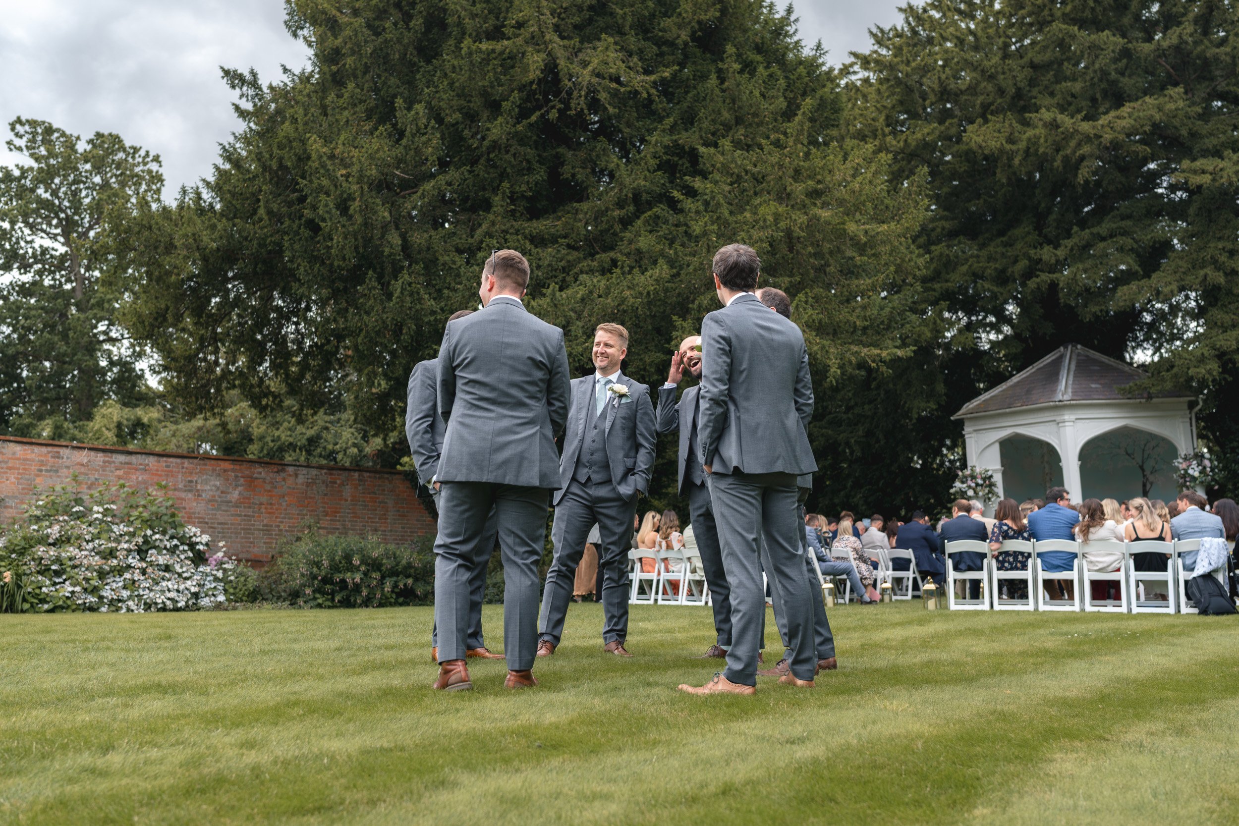 Groom laughing with his groomsmen  on the lawn before an outdoor ceremony at Wasing Park in Berkshire