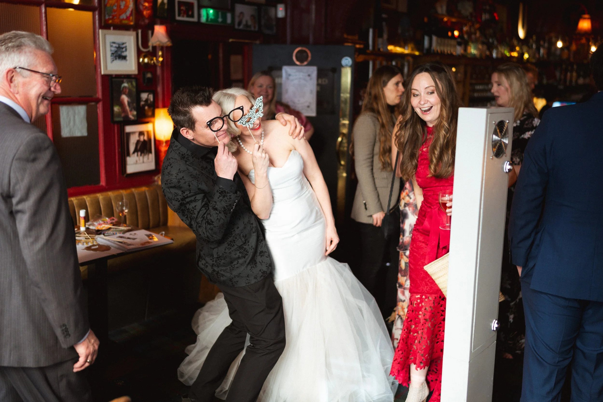 Bride and groom posing with glasses masks in a photo booth at their reception at The Union Club in Soho, London