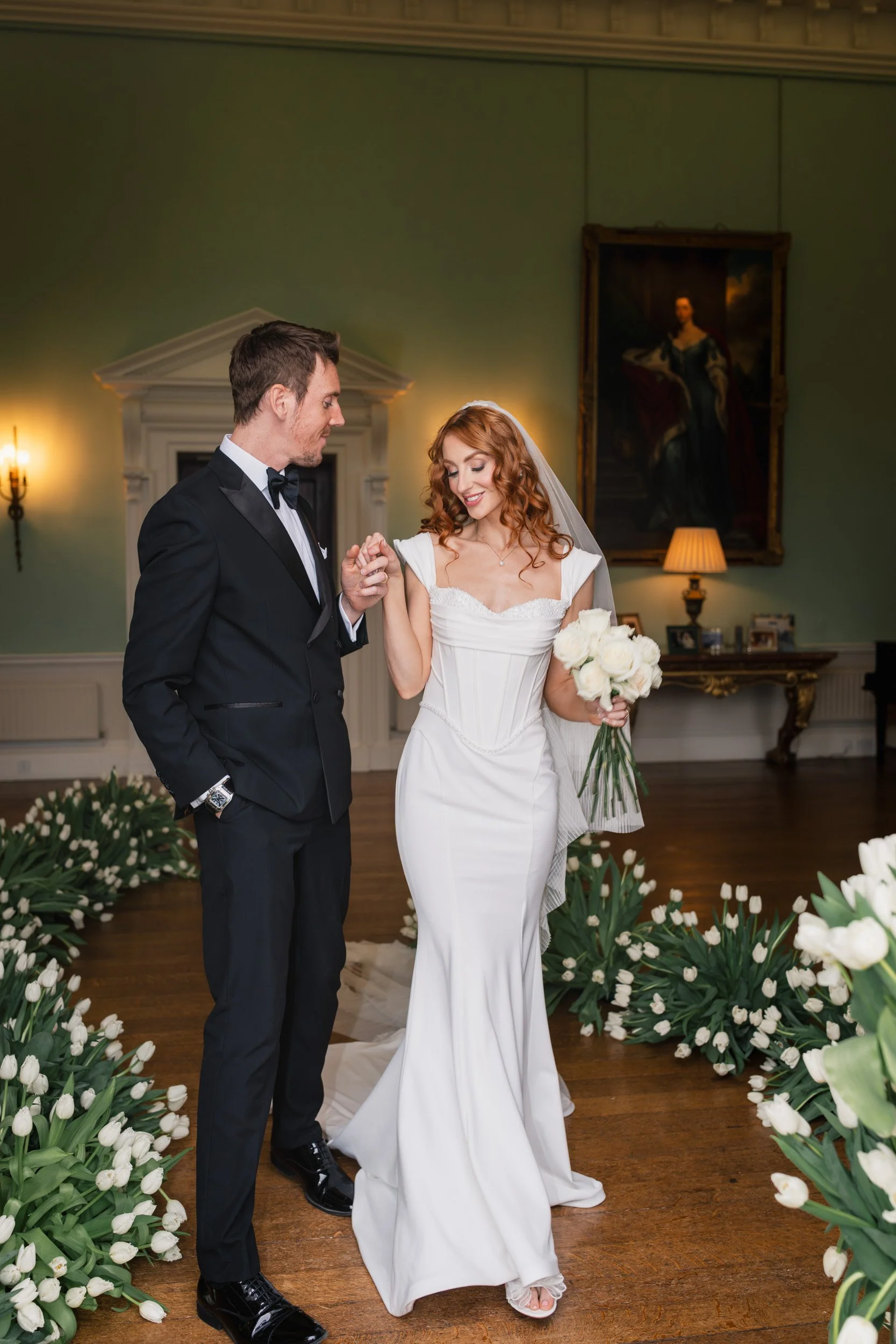 Bride and groom walking hand in hand through a tulip-lined aisle during their reception at Kirtlington Park in Oxfordshire