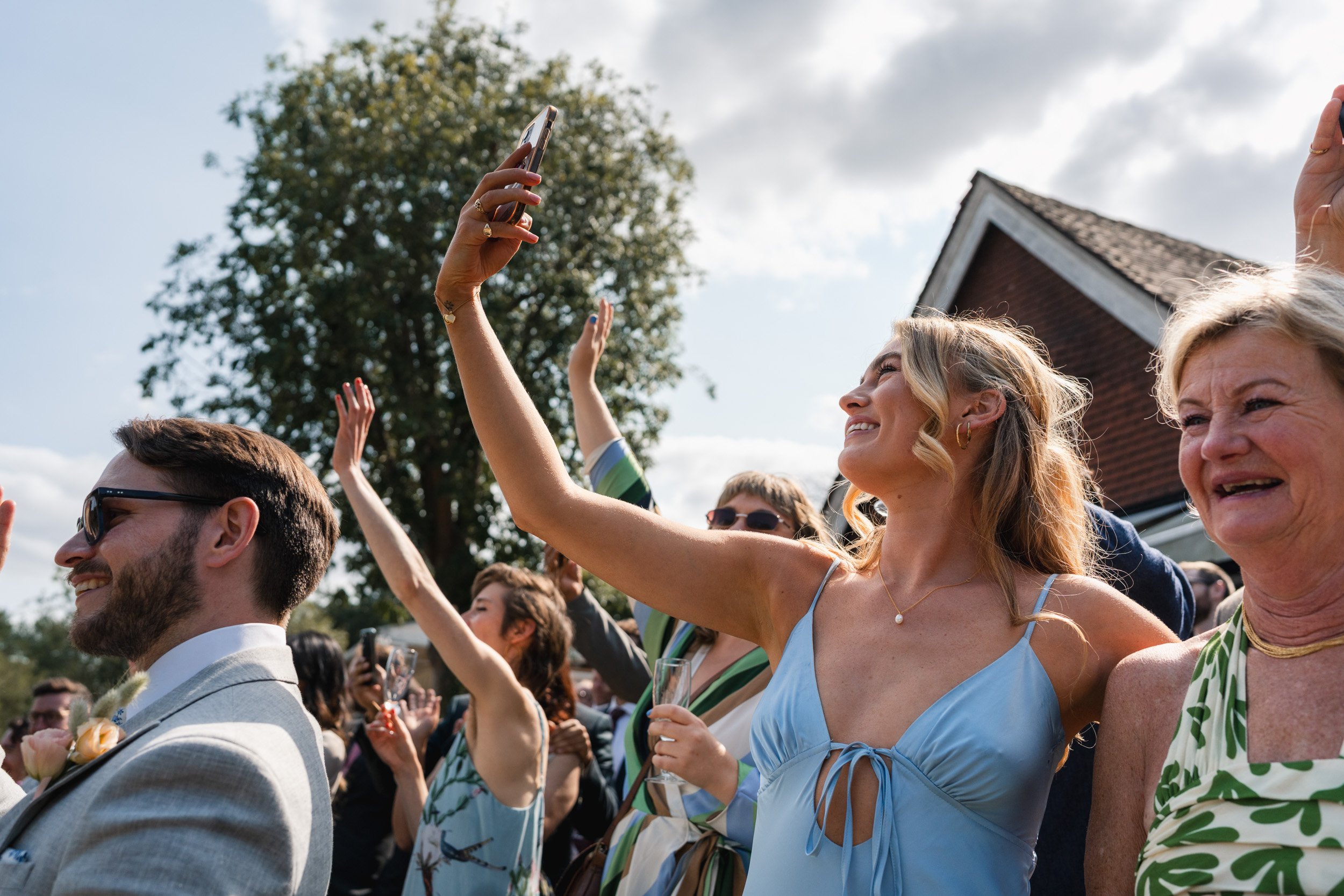 Wedding guests cheering and filming as the  bride and groom arrive by punt boat at Cherwell Boathouse in Oxford 