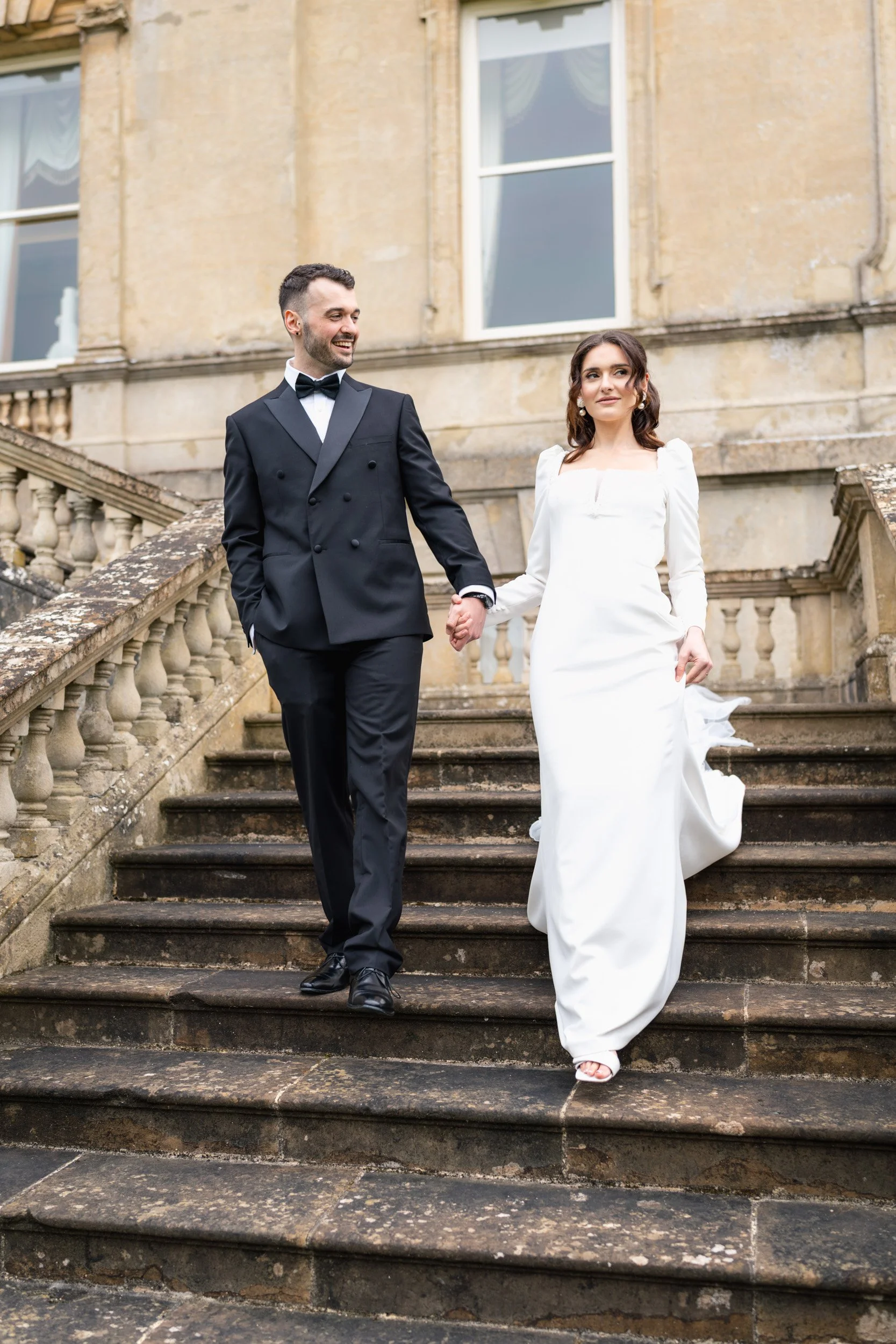 Bride and groom walking down the stairs to greet their guests at Kirtlington Park in Oxfordshire
