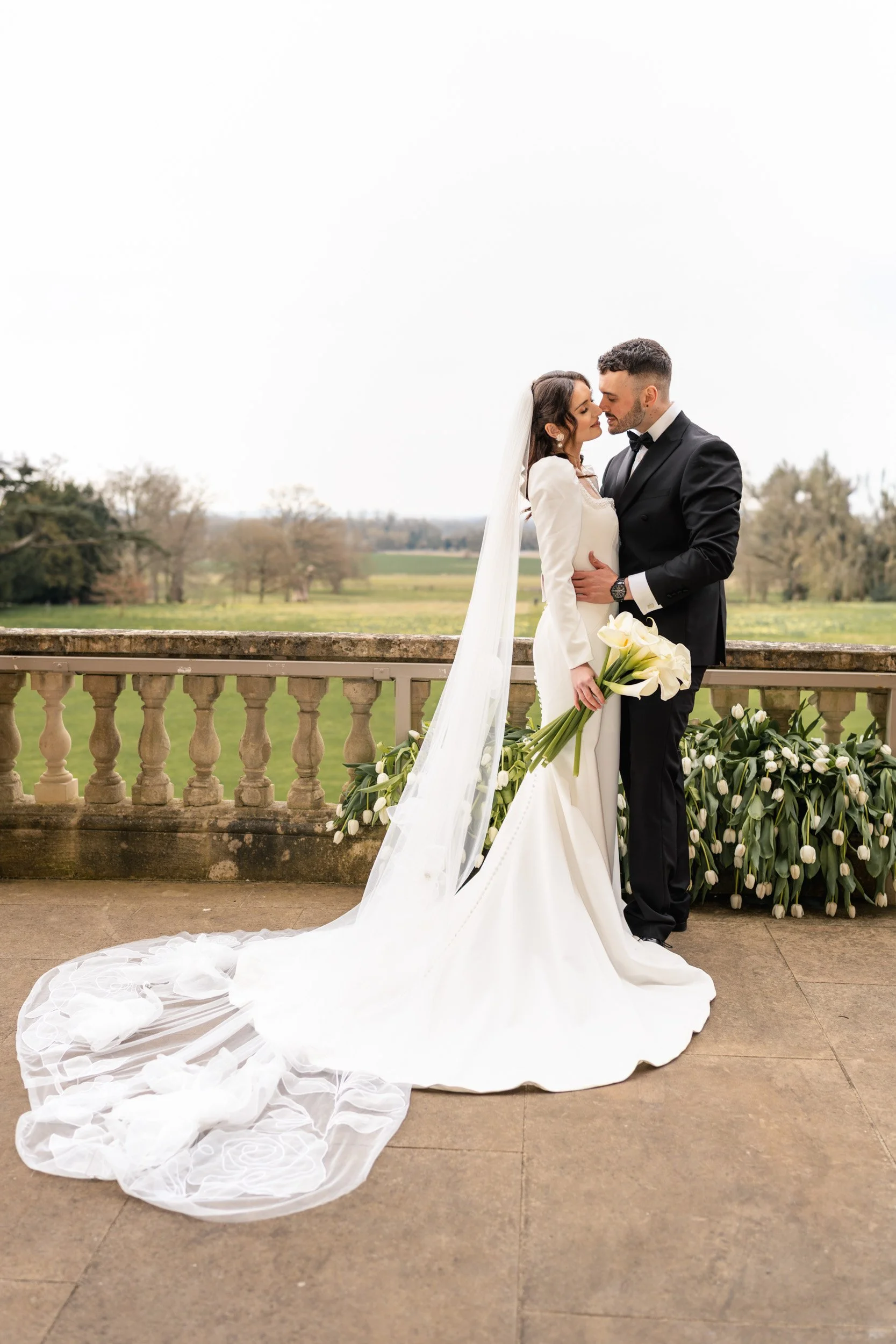 Bride and groom embracing on a floral balcony at Kirtlington Park in Oxfordshire