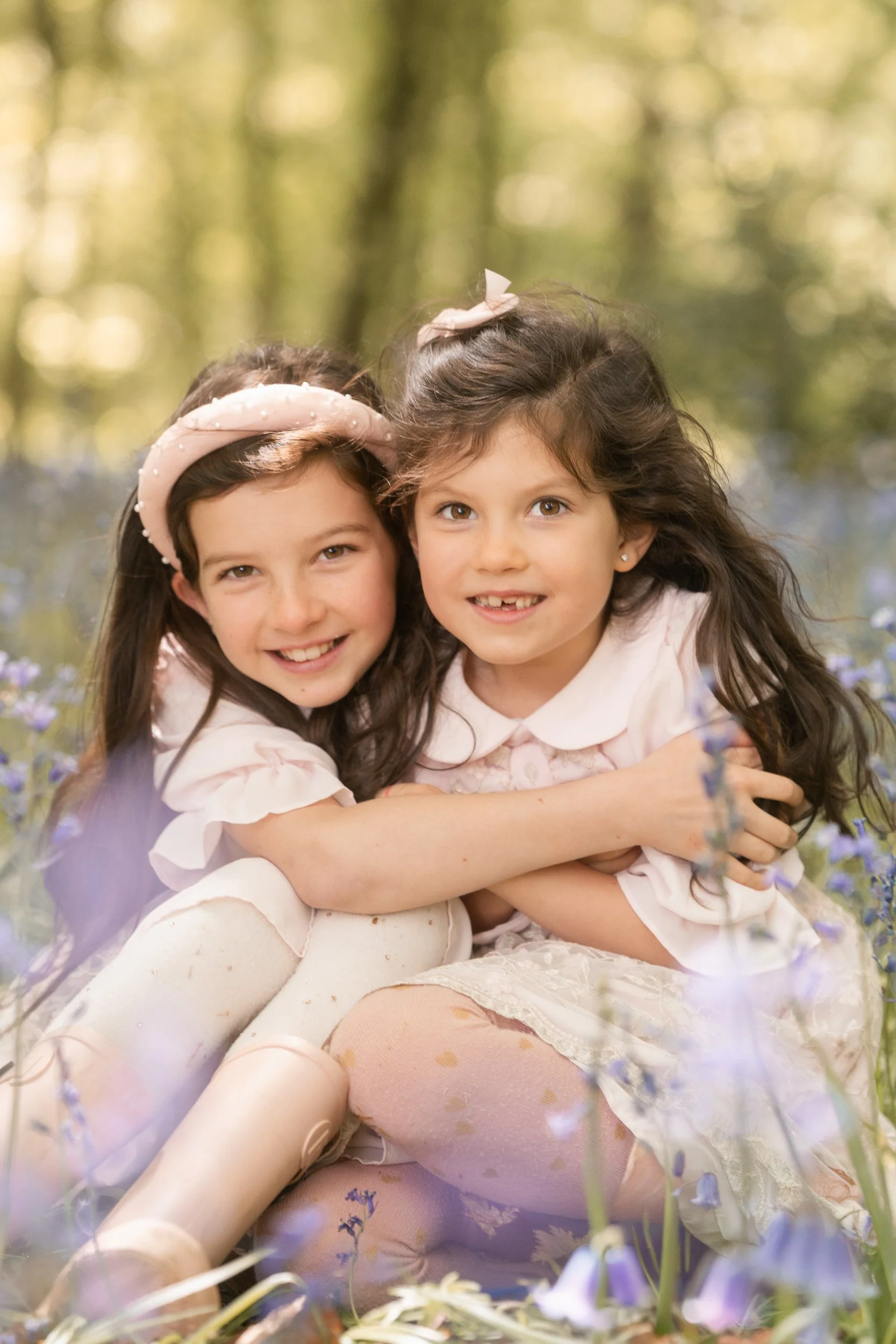 Two young sisters cuddling together during bluebell season in the Chiltern Hills  near Amersham, Buckinghamshire during a family photography session 