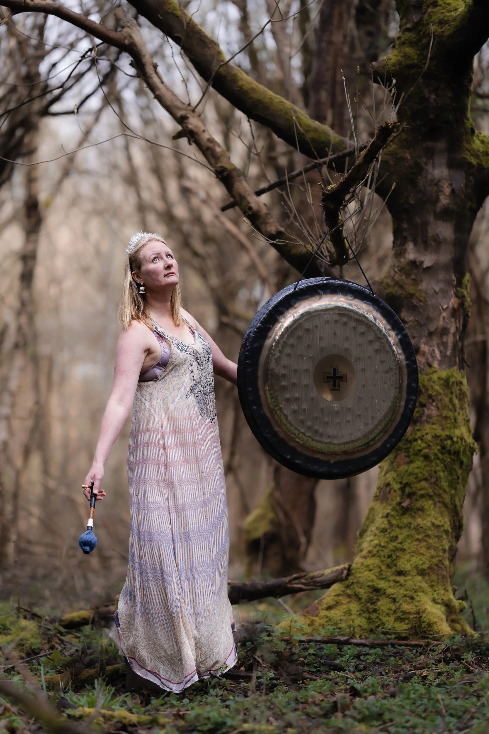 Sound healer standing beside a gong in the woodland during a sound healing session in Amersham Buckinghamshire