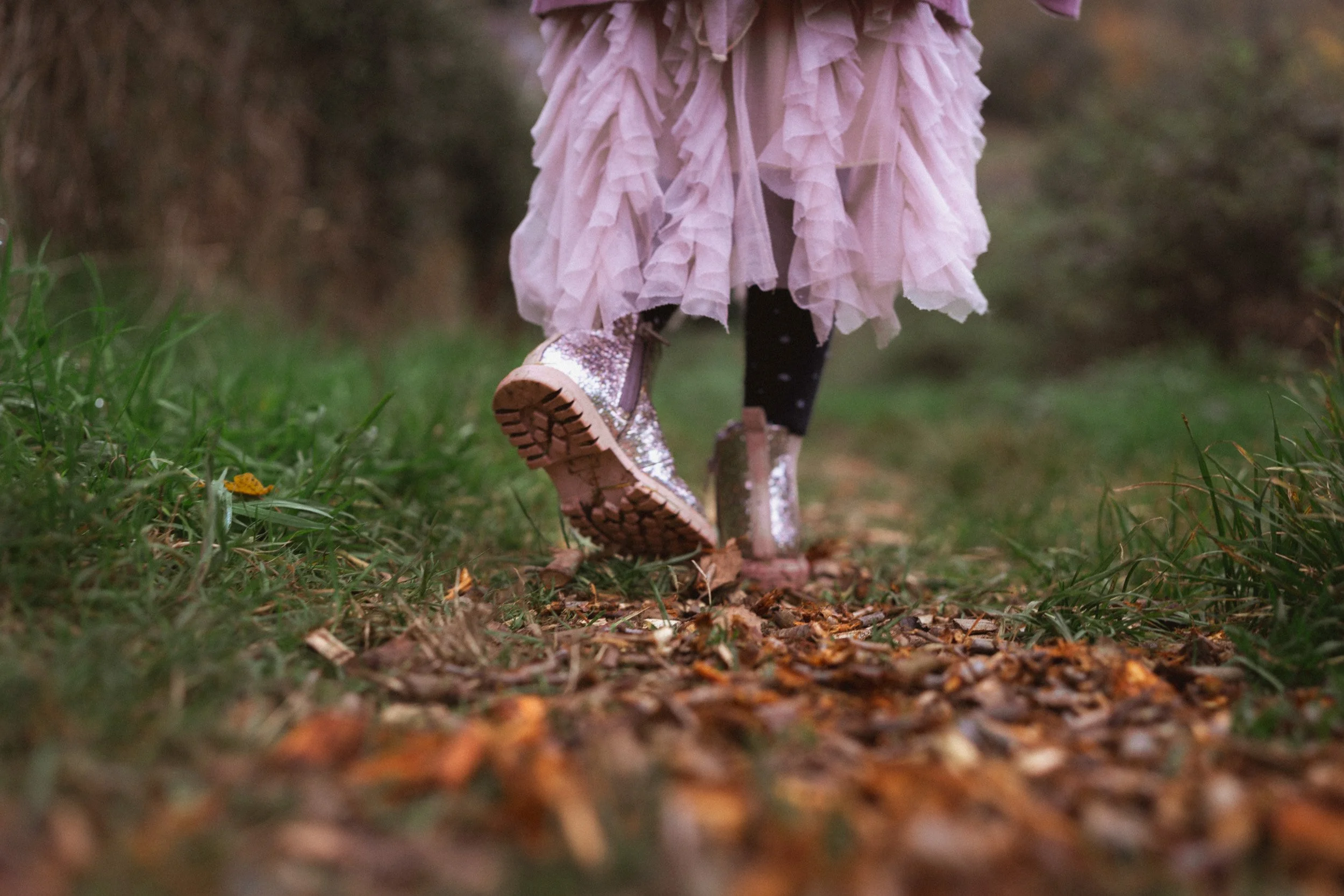 Close up of a young girl in a pink dress and pink shoes kicking the autumn leaves in a relaxed outdoor family photography session in the countryside near Thame, Oxfordshire