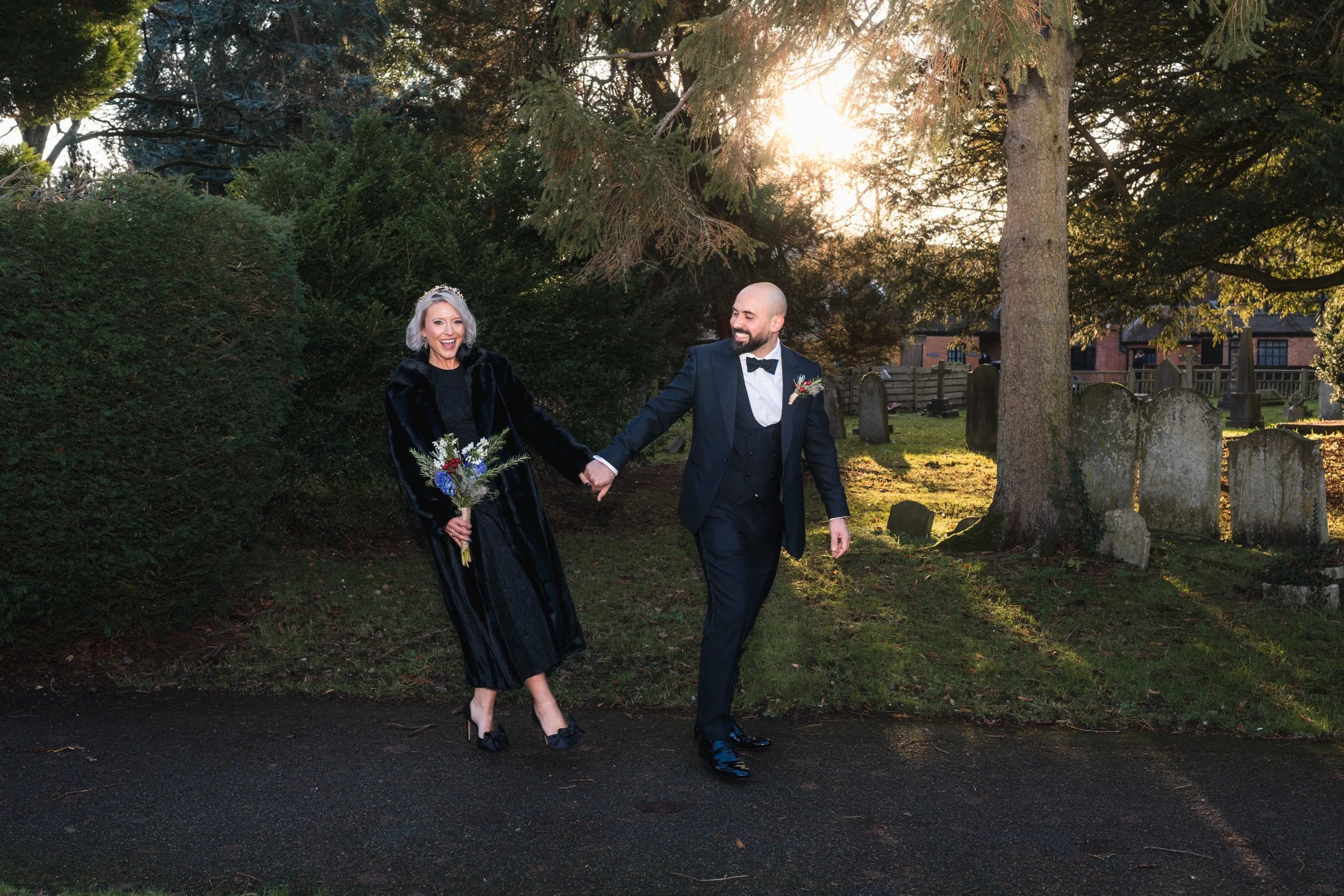 Groom leading his bride through the grounds of the the church in Old Beaconsfield Buckinghamshire before their wedding ceremony