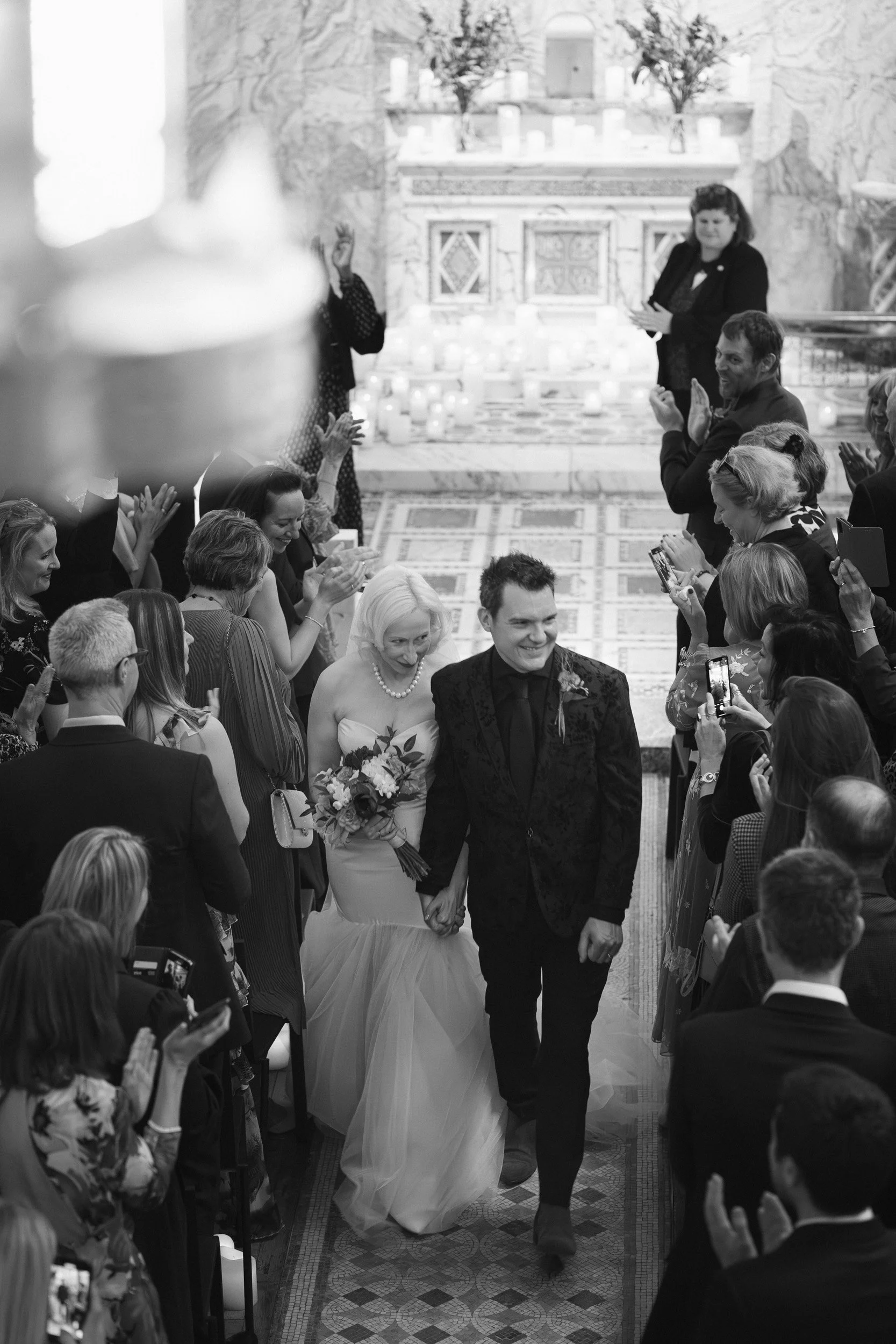 Bride and groom walking down the aisle as guests applaud at Fitzrovia Chapel in London