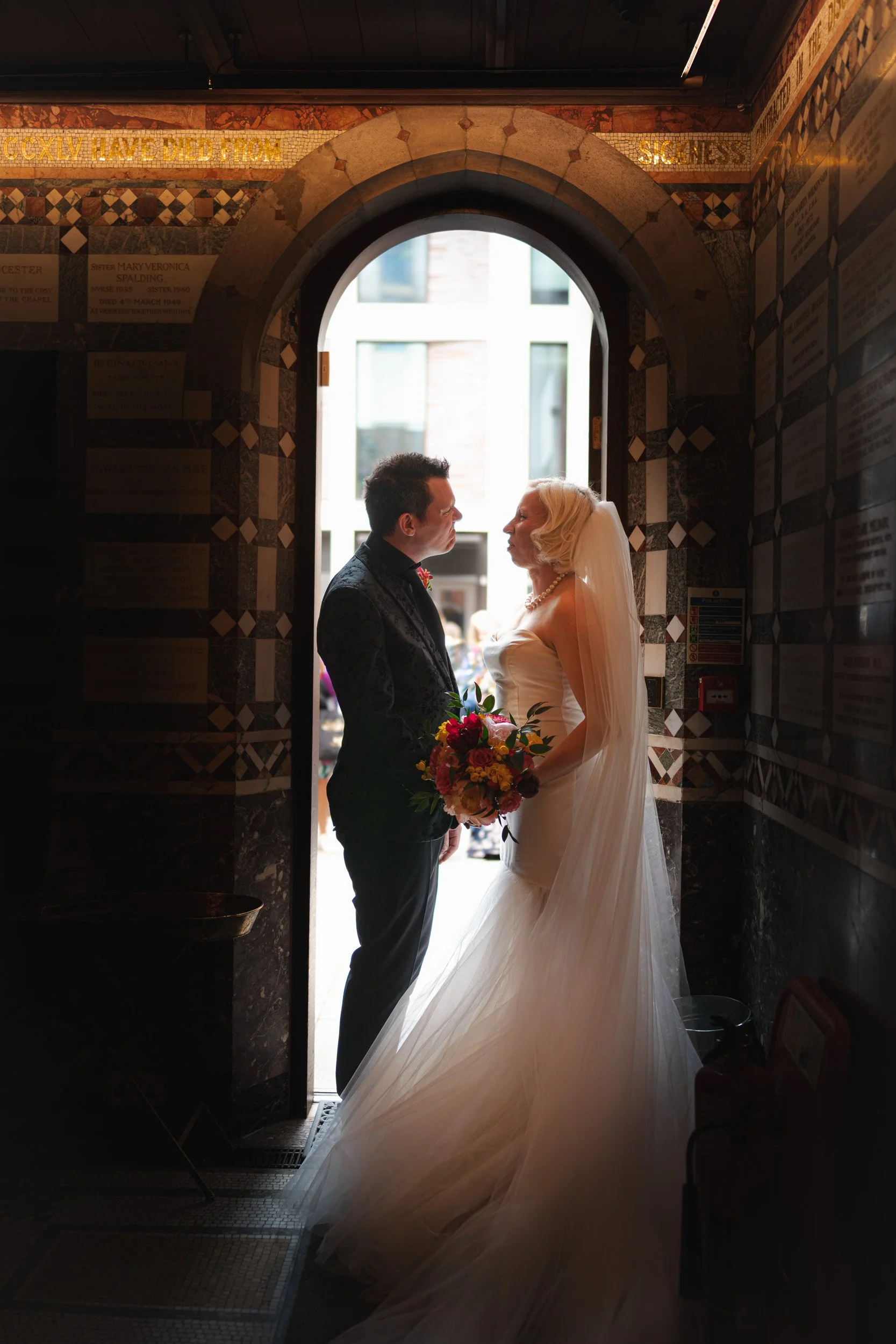 Bride and groom pull cheeky faces in the doorway of Fitzrovia Chapel in London