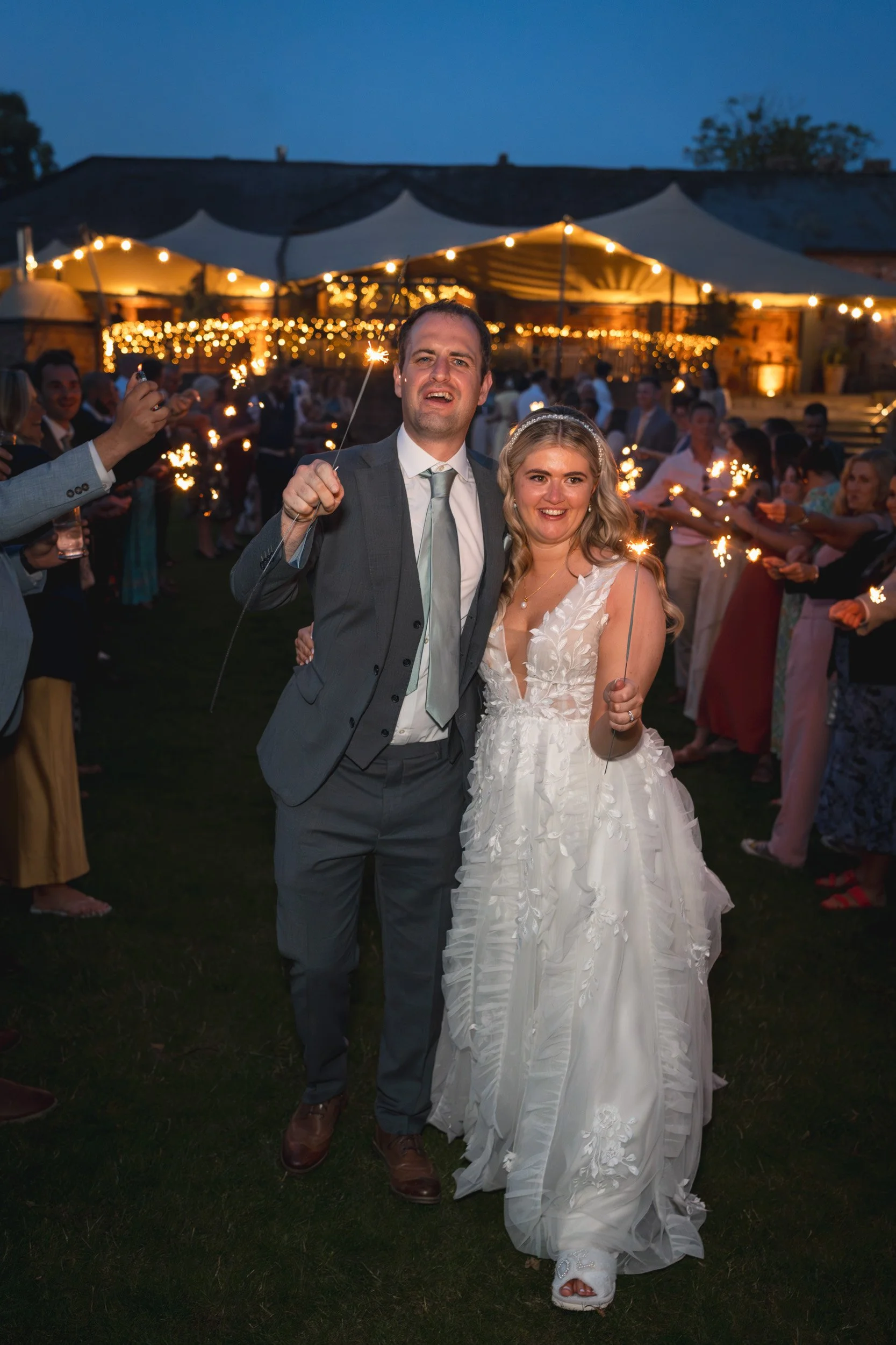 Bride and groom smiling holding  sparklers with their wedding guests at the end of their wedding reception at Wasing Park in Berkshire