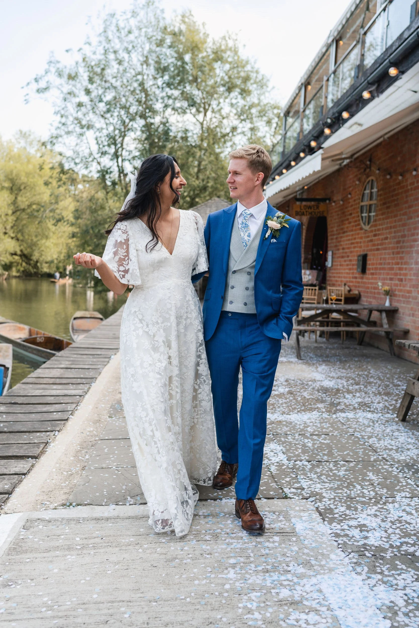 Bride and groom walking arm in arm and gazing at each other outside Cherwell Boathouse in Oxford 