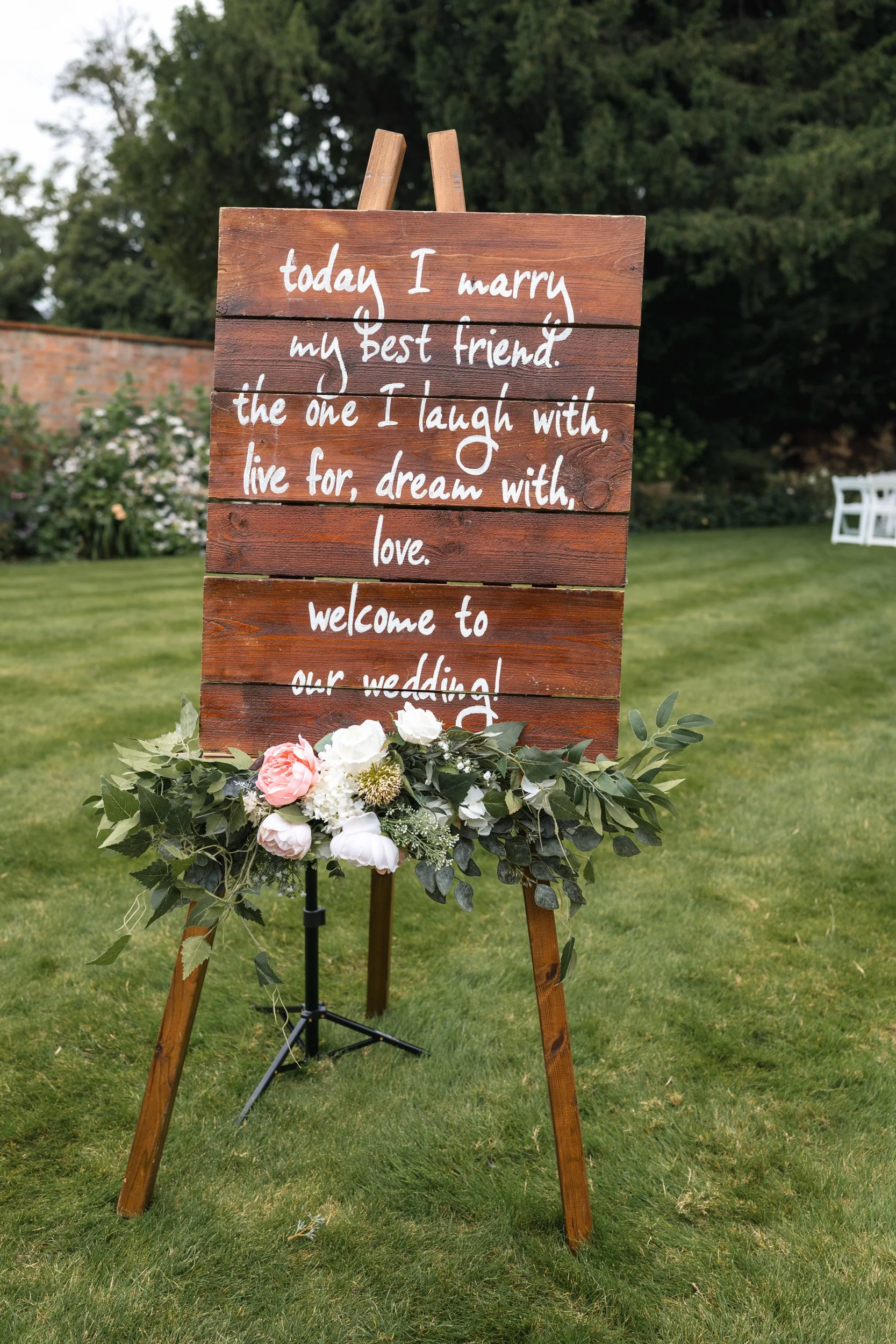Wooden  wedding welcome sign with floral display  greeting guests to a ceremony in the gardens of Wasing Park, Berkshire