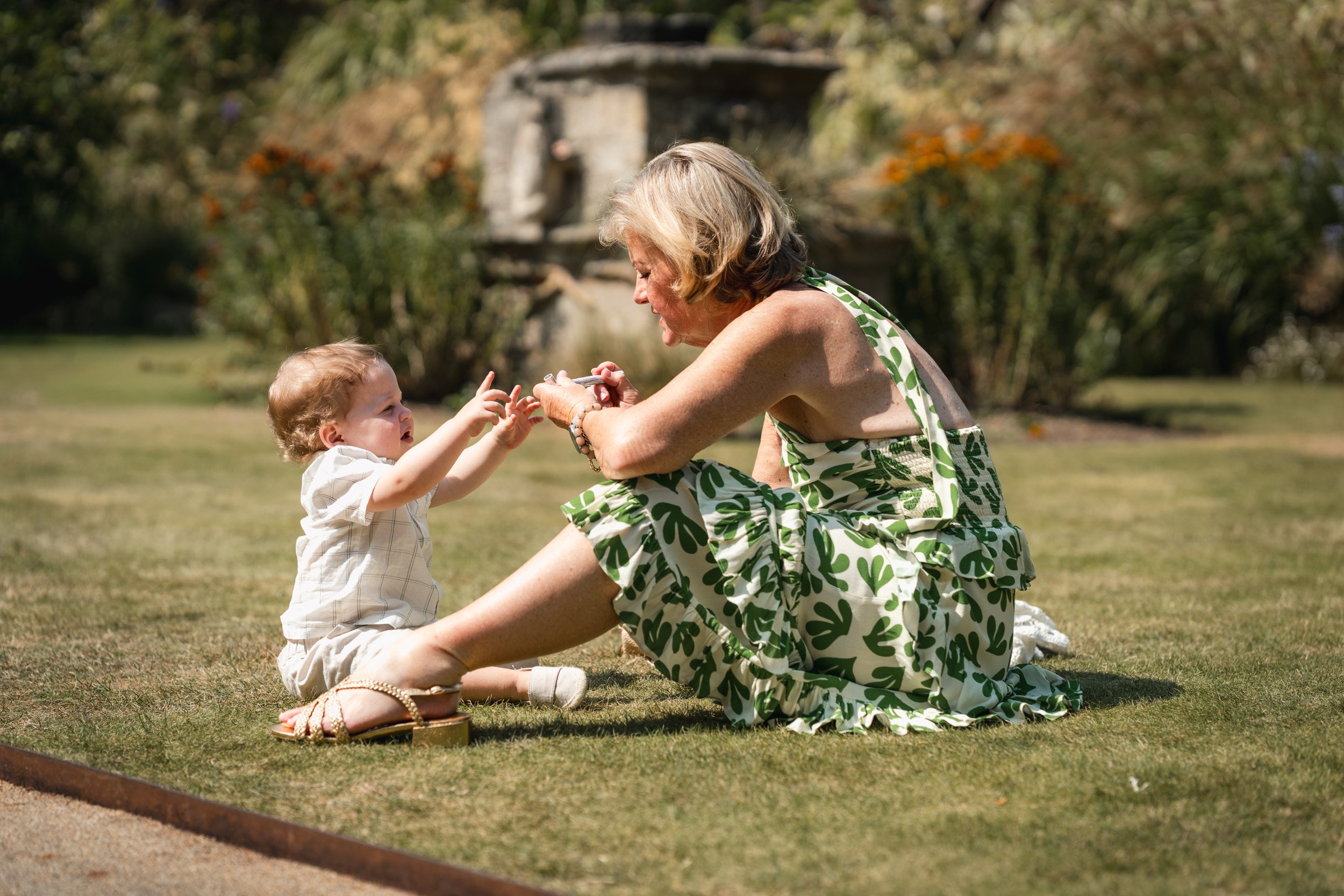 Grandmother playing with her grandson on the grass of a historic  garden after a wedding ceremony at Oxford University college in  Oxford, England