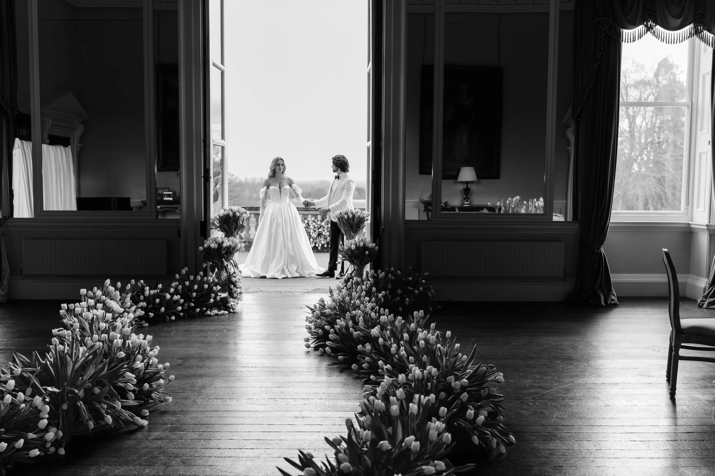 Bride and groom holding hands in the doorway with tulip lined aisle leading to the wedding reception at Kirtlington Park in Oxfordshire