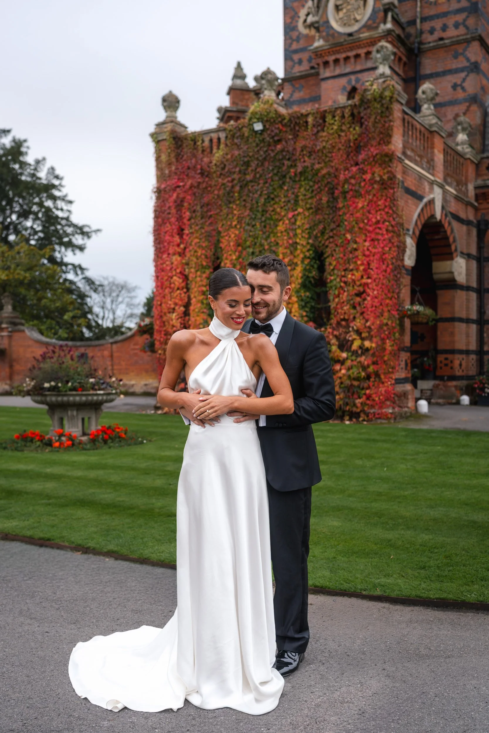 Bride and groom embracing outside The Elvetham Hotel in Hampshire with ivy-covered red brick architecture behind them 
