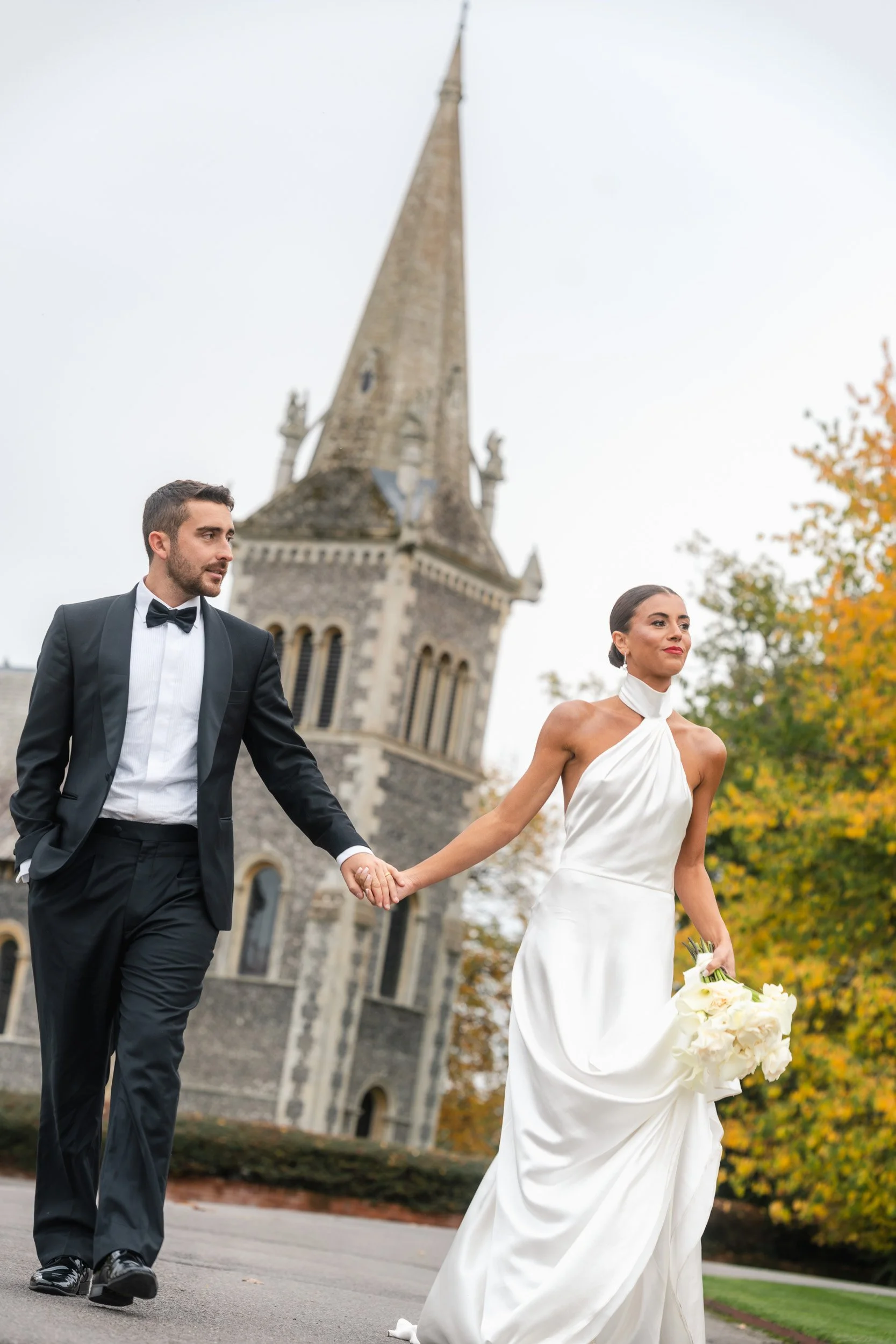Bride and groom walking hand in hand in front of The Bell Tower at The Elvetham Hotel in Hampshire