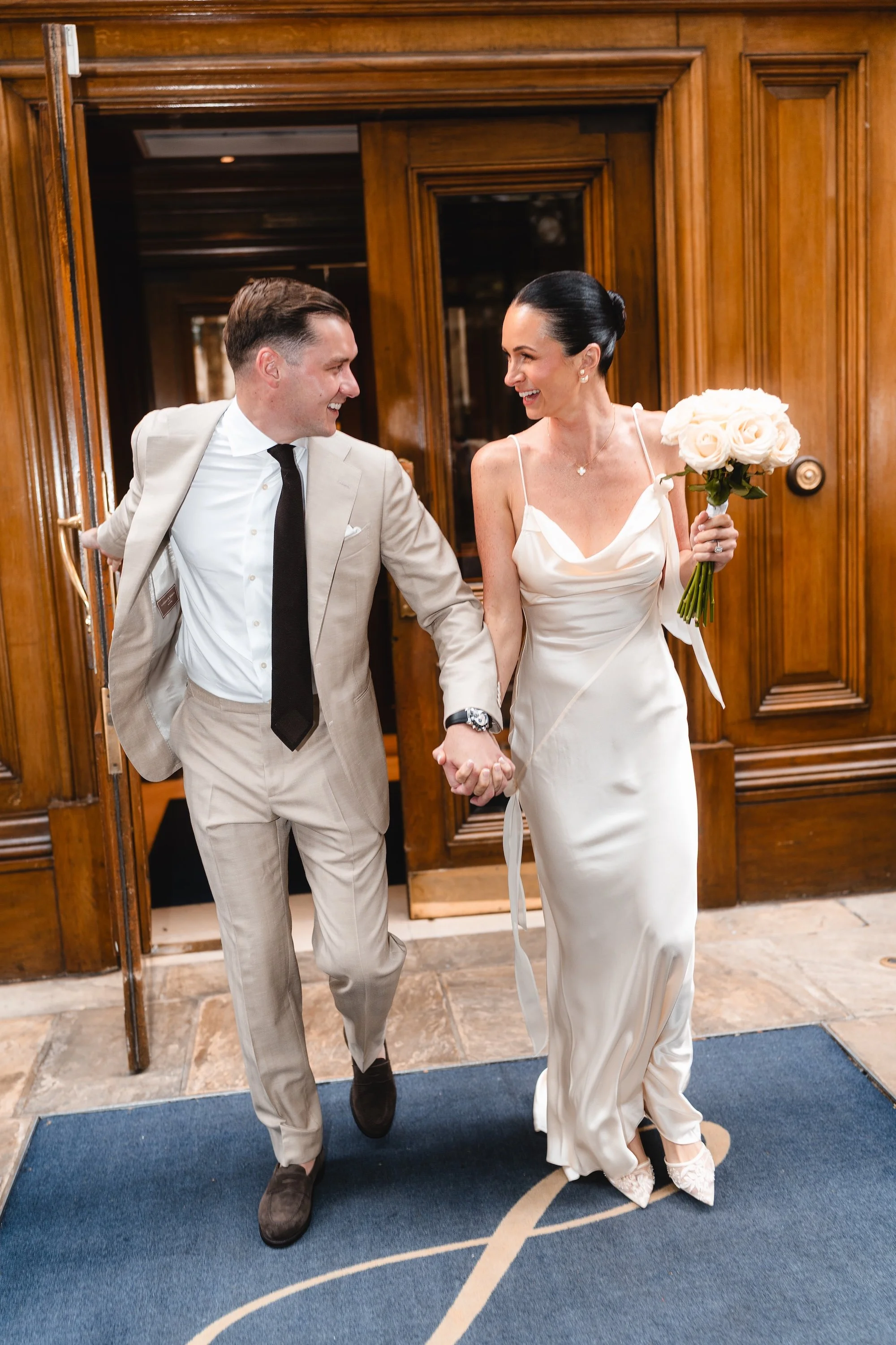 Bride and groom laughing holding hands as they leave The Landmark London ready to walk to their Old Marylebone Town Hall wedding for their London Micro wedding