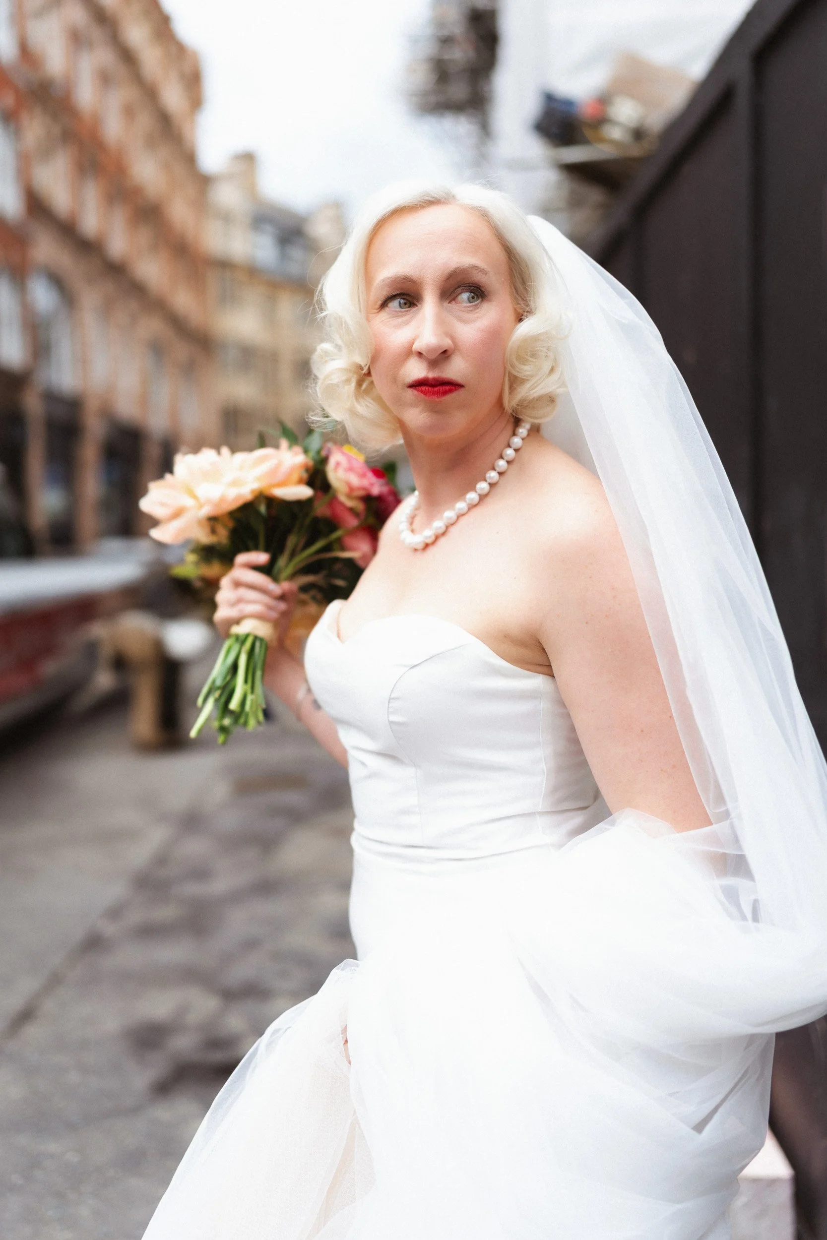 Bride holding her veil and flowers as she hurries through Soho Streets after her wedding ceremony at Fitzrovia Chapel 
