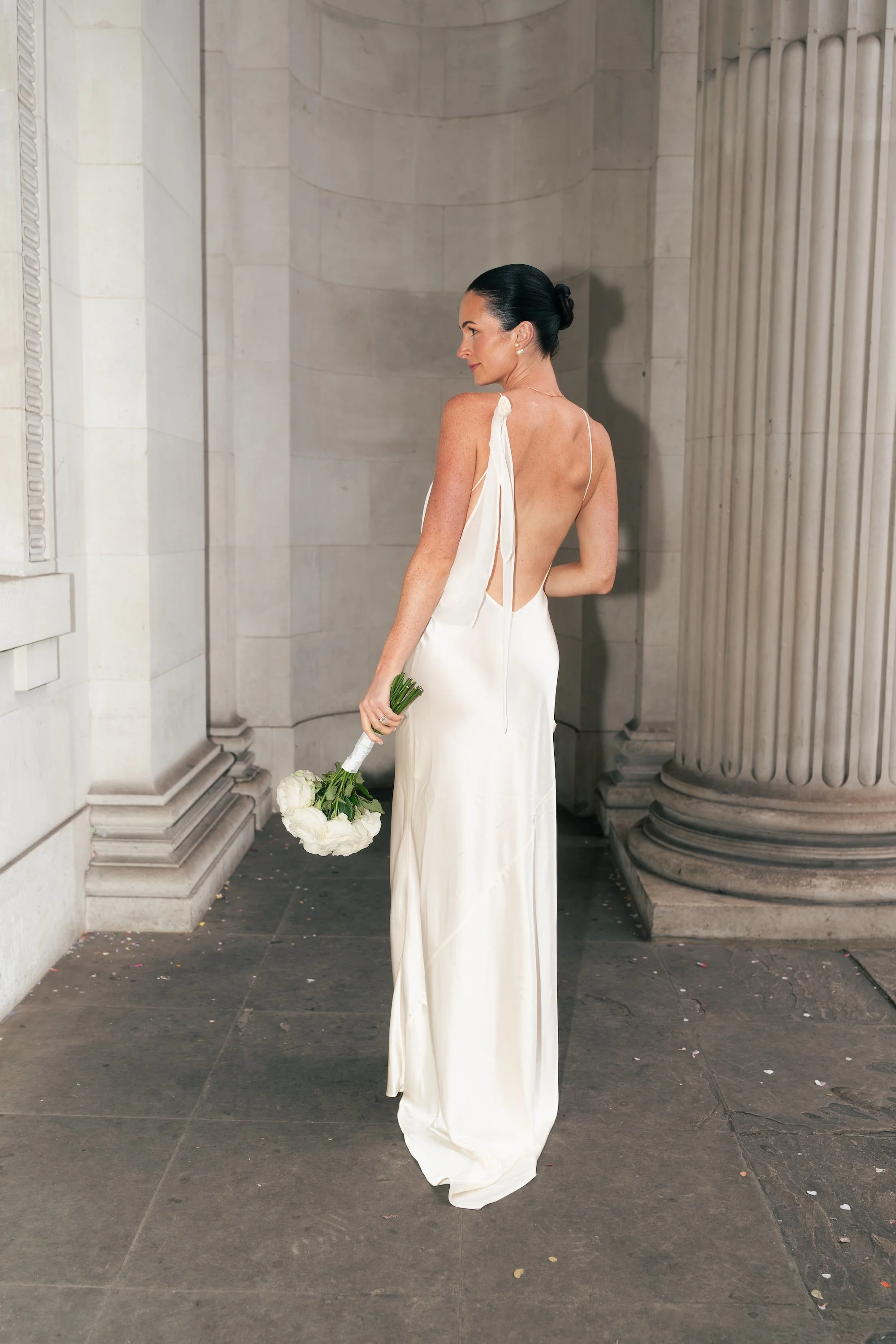 Bride in a white backless wedding dress, beneath the iconic columns outside Old Marylebone Town Hall before her intimate London wedding ceremony