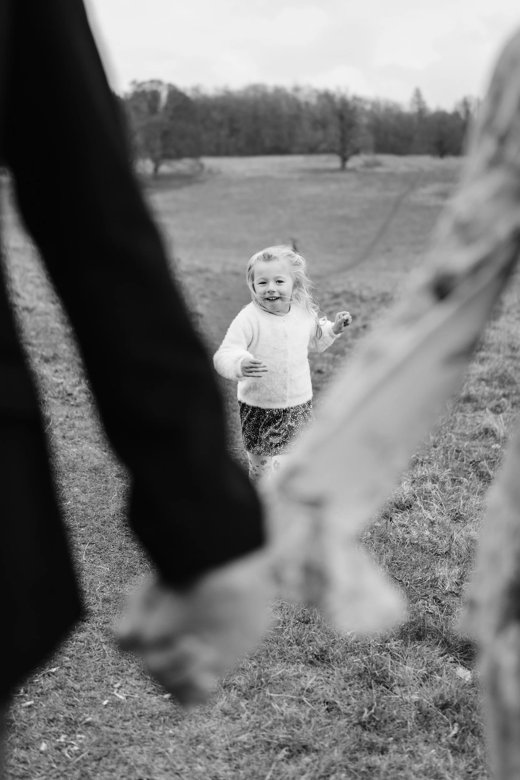 a young girl runs smiling towards her parents,. She is in focus and her parents hands are holding softly out of focus for a family photoshoot in Great Missenden in Buckinghamshire