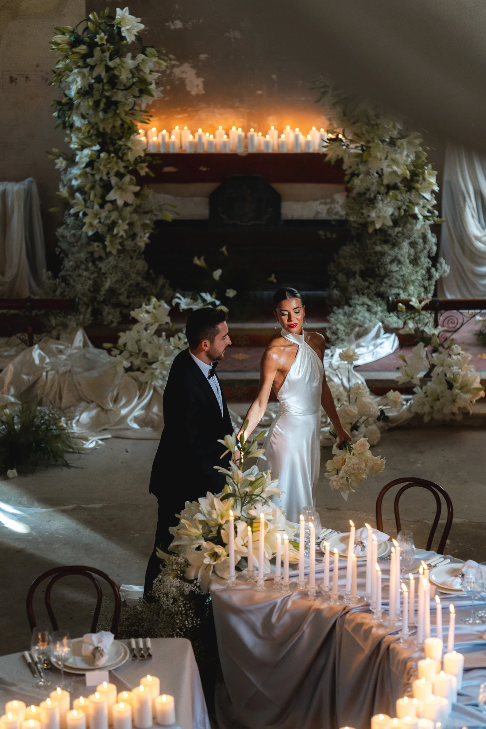 Bride and groom walking through a candlelit reception room with draped fabric and floral displays inside The Bell Tower at The Elvetham Hotel in Hampshire