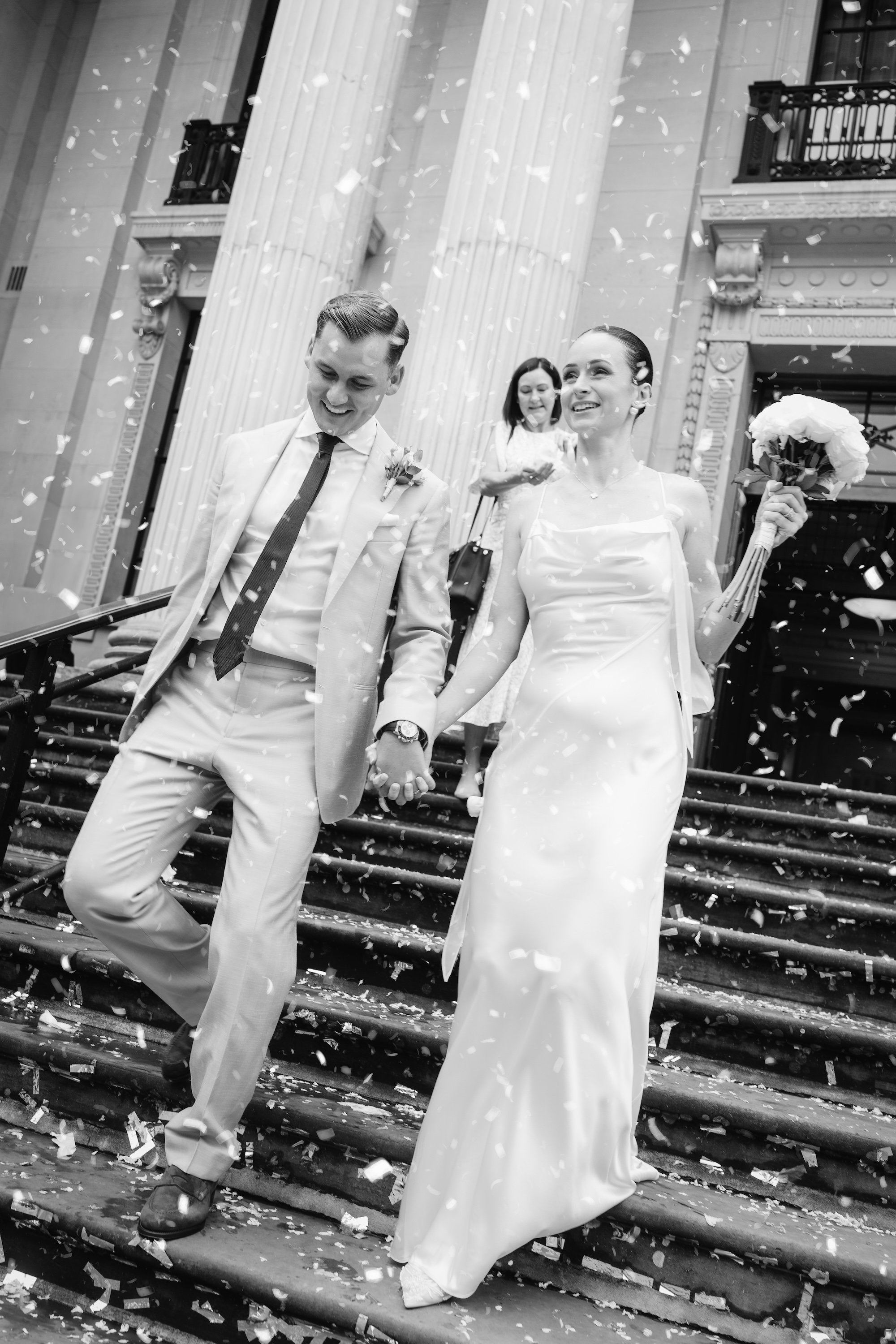 Bride and groom smiling as they walk though the confetti on the steps of Old Marylebone Town Hall after their  micro wedding
