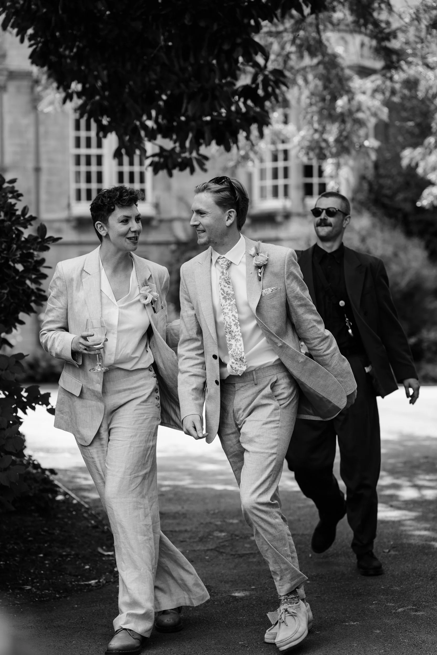 Groomsmen laughing and walking through the gardens after a wedding ceremony at Oxford University college in  Oxford, England