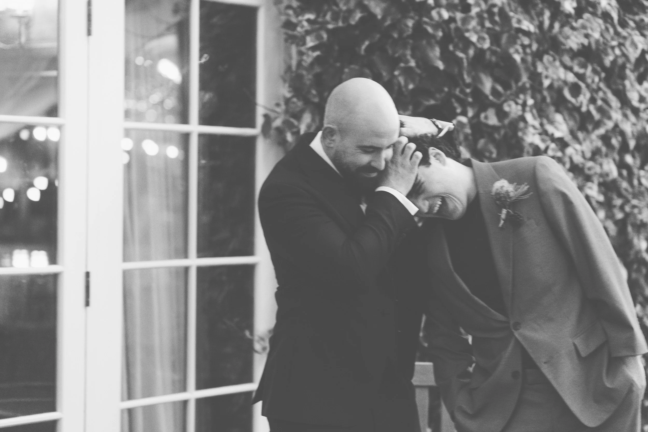 Groom playfully holding his younger brother in a headlock while they laugh together  during an evening wedding reception at The Bedford Arms in Chenies, Buckinghamshire