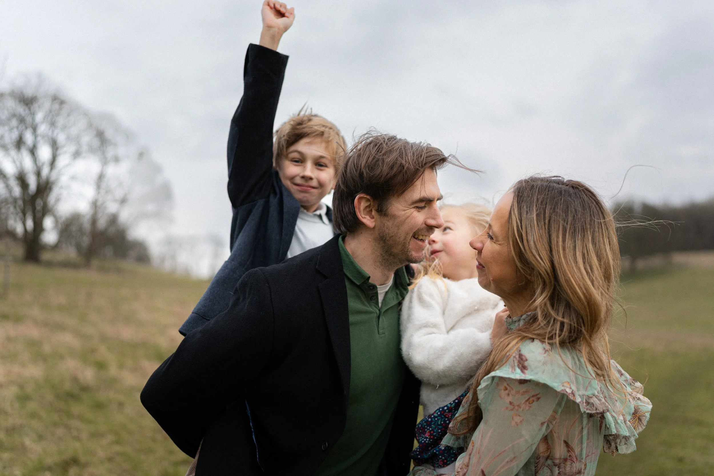 A young family of 4 laughing and cuddling in a field in Great Missenden Buckinghamshire at golden hour for a family photoshoot