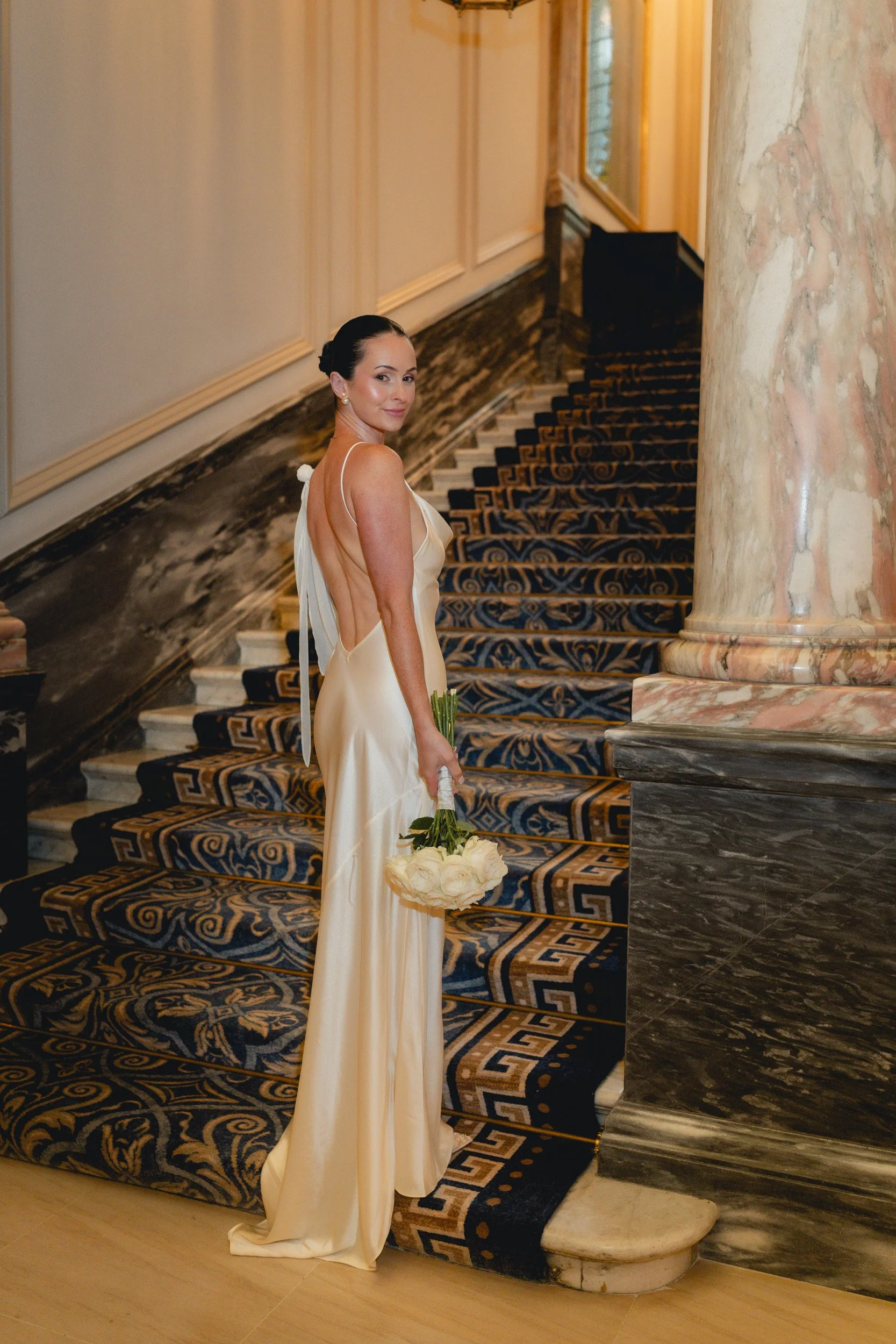 Bride standing on the grand staircase holding her bouquet at The Landmark Hotel,  London in Marylebone