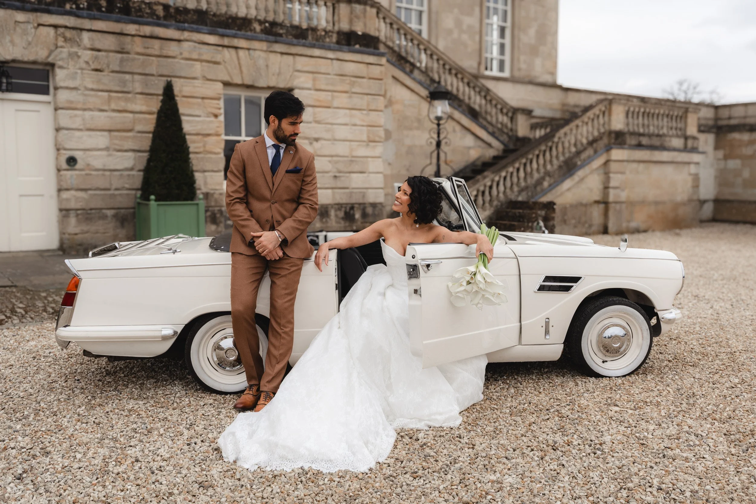 Bride and groom setting off in a vintage white wedding car at Kirtlington Park in Oxfordshire