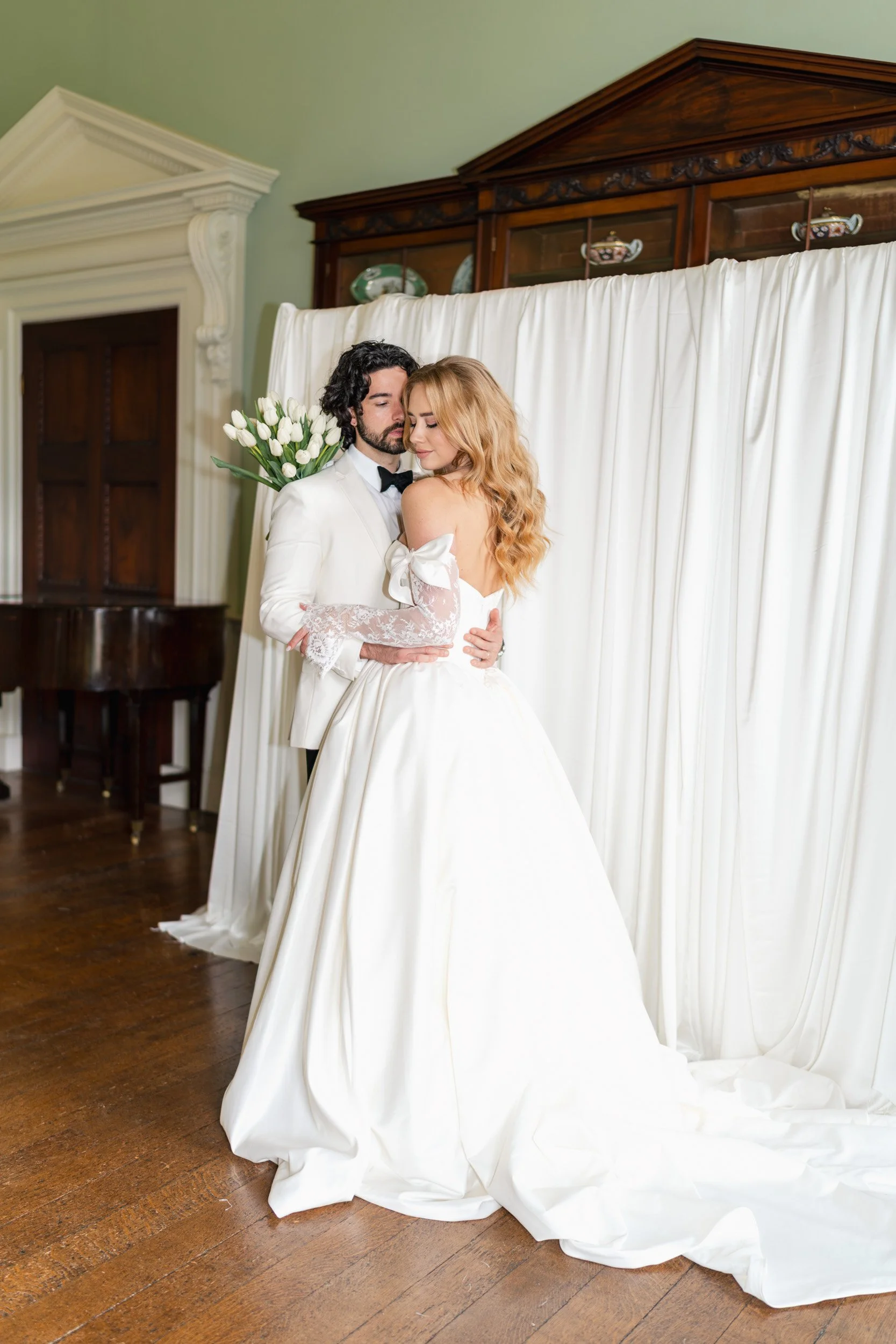 Close up of a ride and groom hugging in front of a white backdrop with tulip-lined reception floor at Kirtlington Park in Oxfordshire