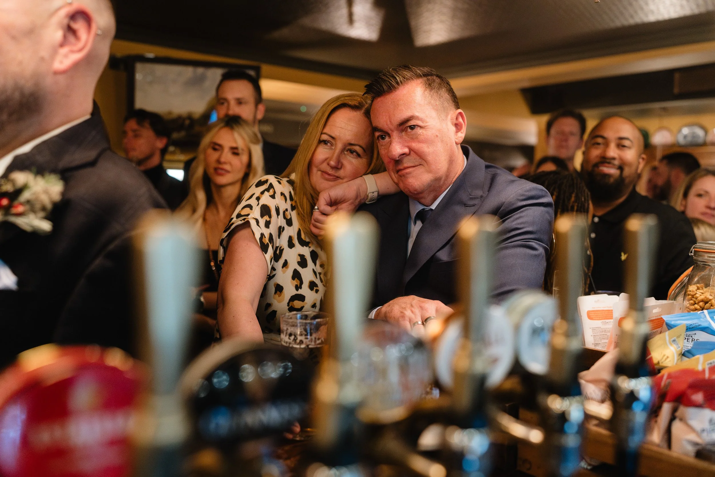 Wedding guests listening and smiling at the bar at a  wedding reception at The Bedford Arms in Chenies 